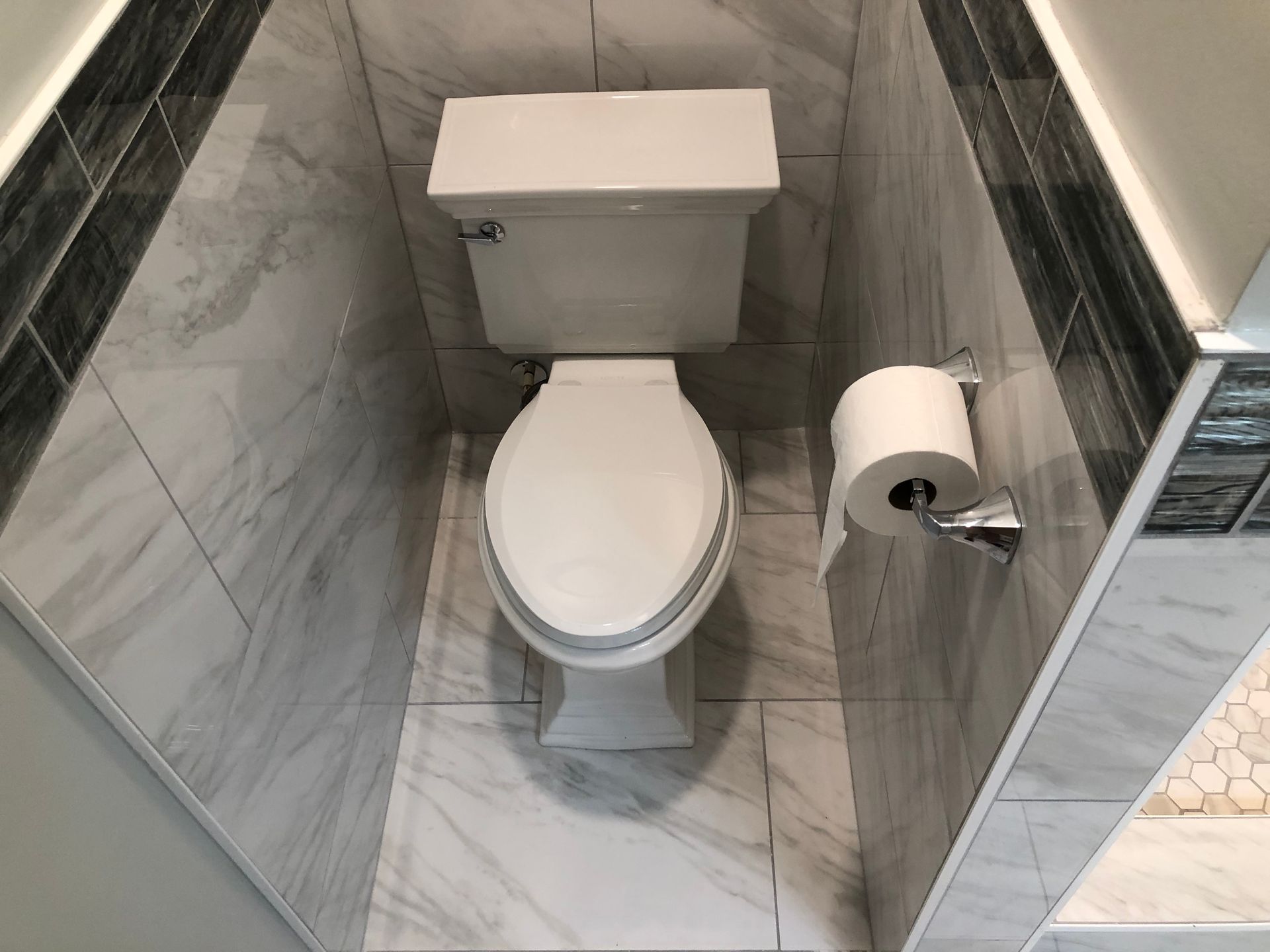Small bathroom with a white toilet and toilet paper holder beside it, set against gray marble-patterned walls.
