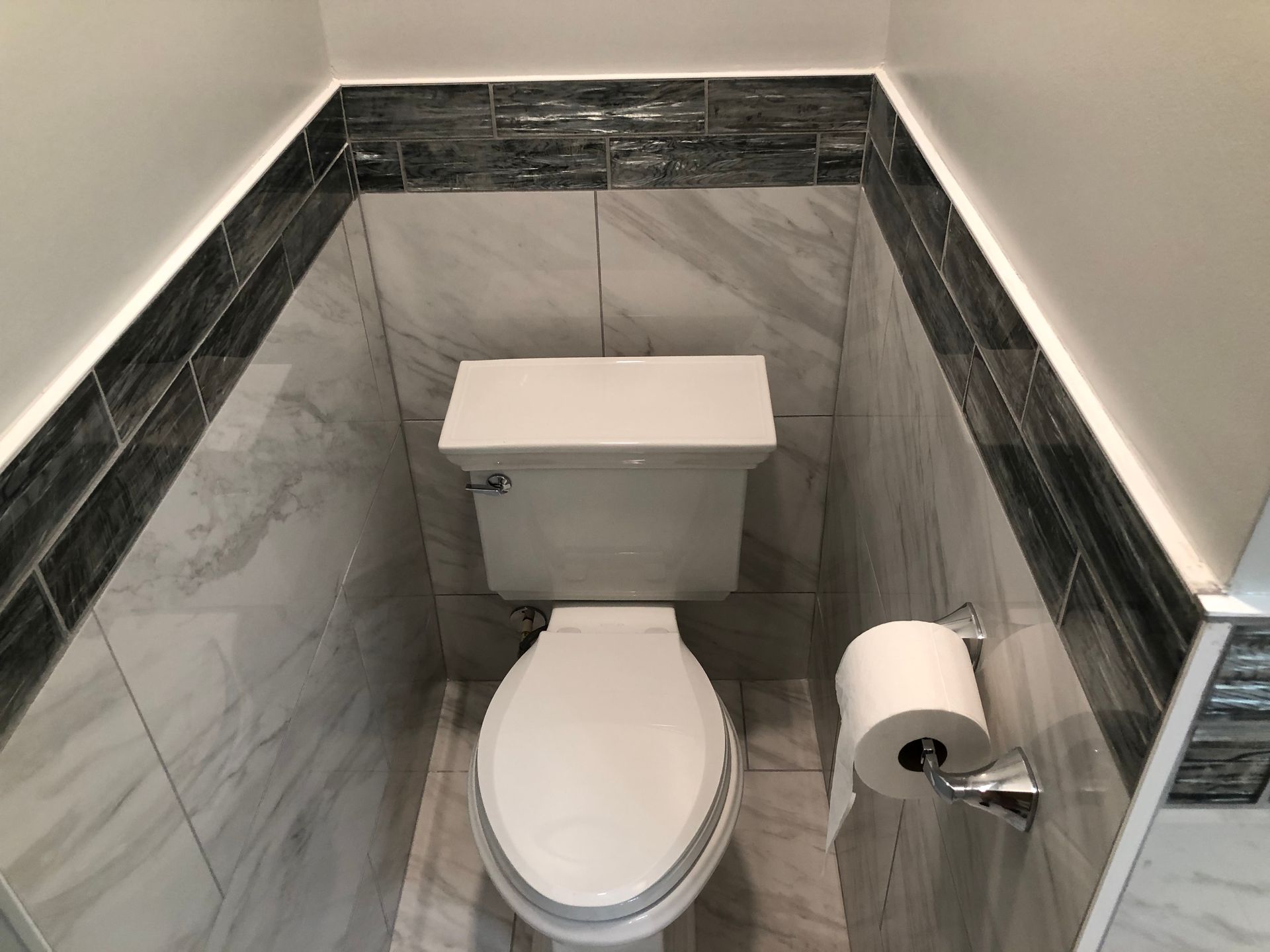 Small bathroom with a white toilet, gray marble tile walls, and a toilet paper roll on the right.