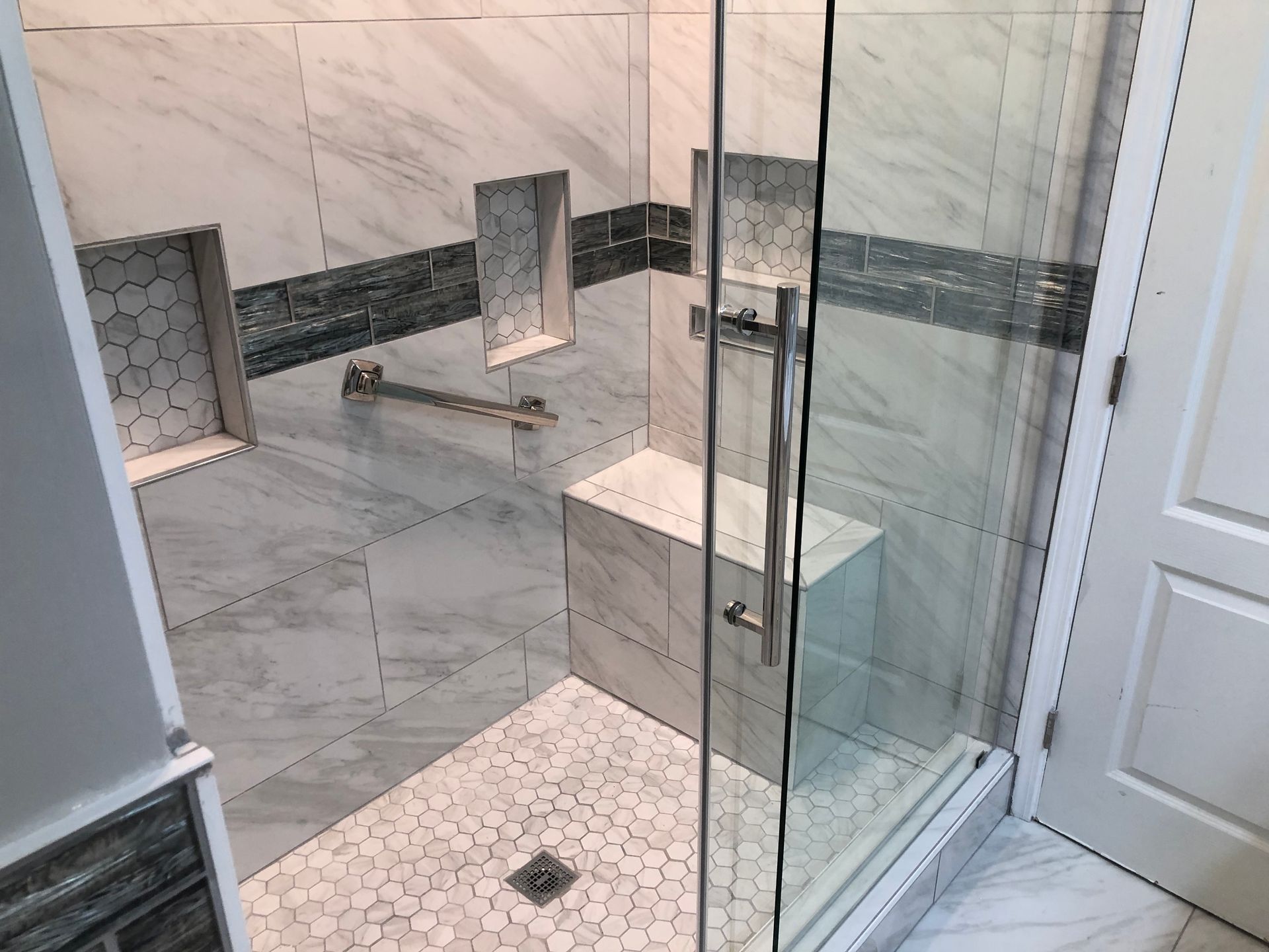 Modern bathroom with glass shower enclosure, marble tile walls, and white floor tiles.