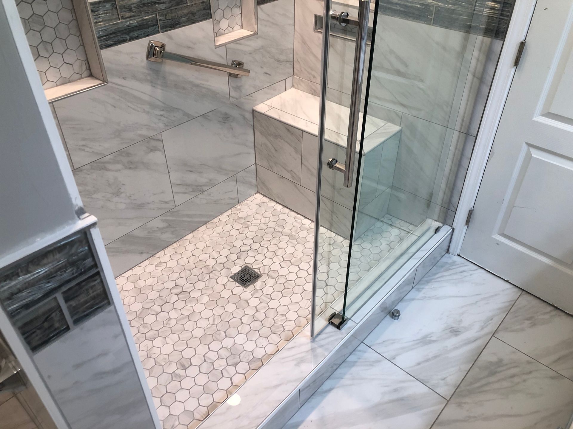 Bathroom with glass shower enclosure, white marble tile, and hexagonal mosaic shower floor