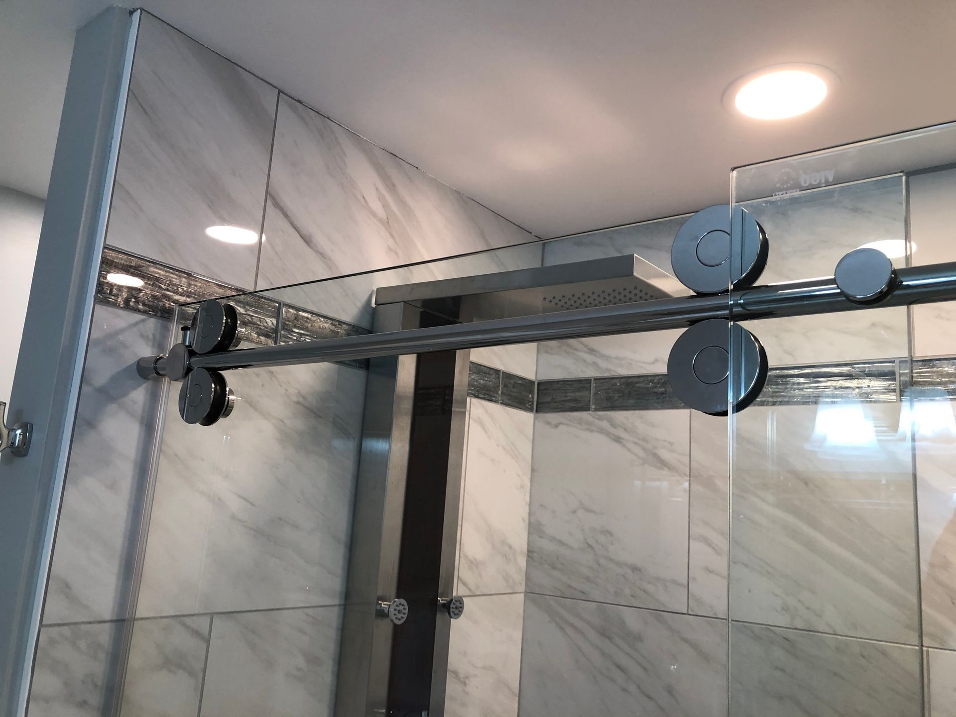 Glass shower enclosure with metal hardware and marble-tile walls in a modern bathroom
