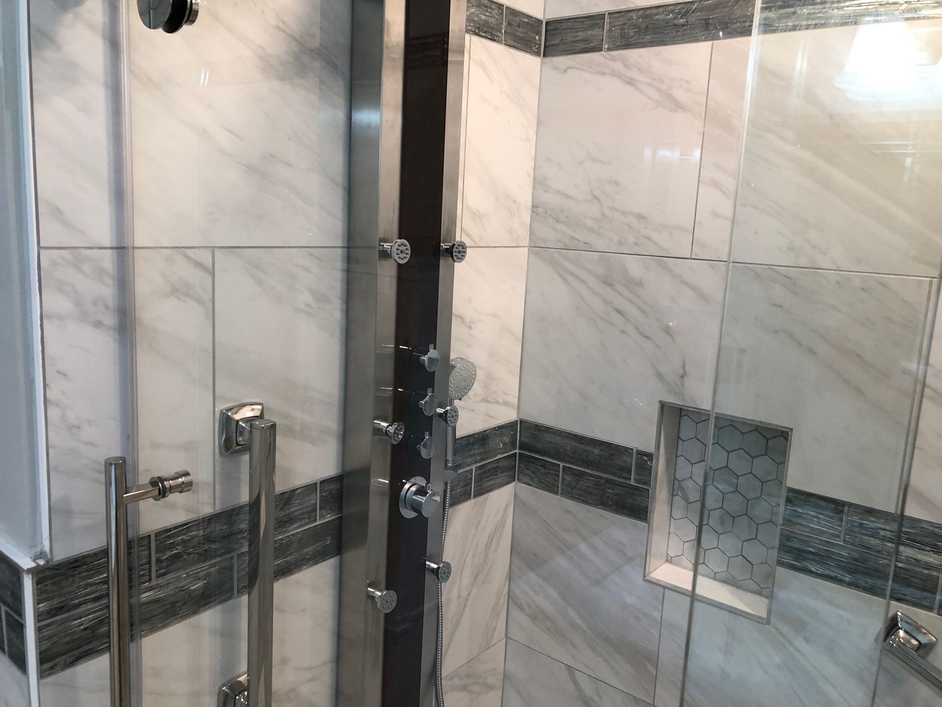 Modern glass shower with chrome fixtures and marble tile walls