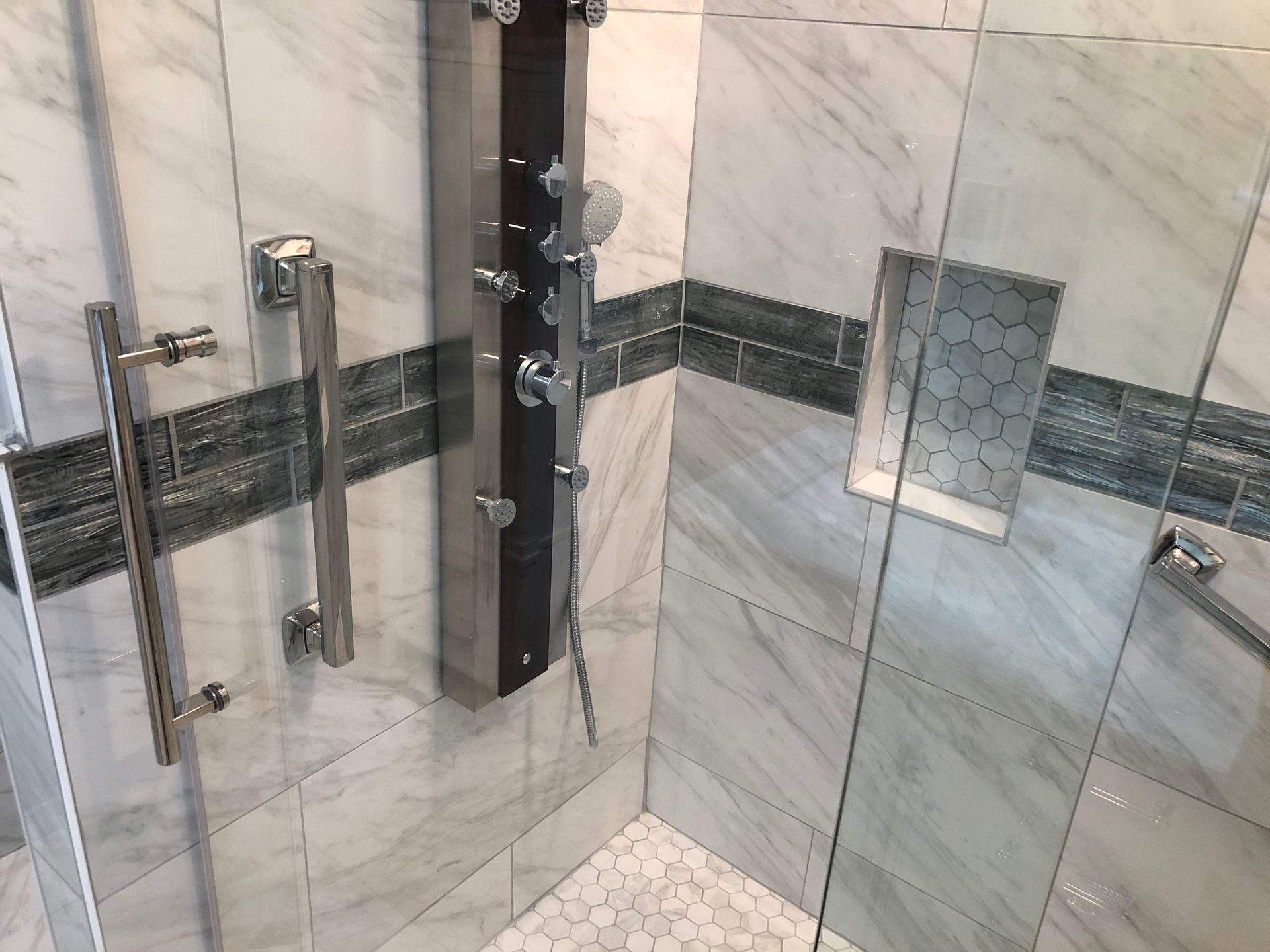 Glass shower with marble tile and chrome grab bars in a tiled bathroom