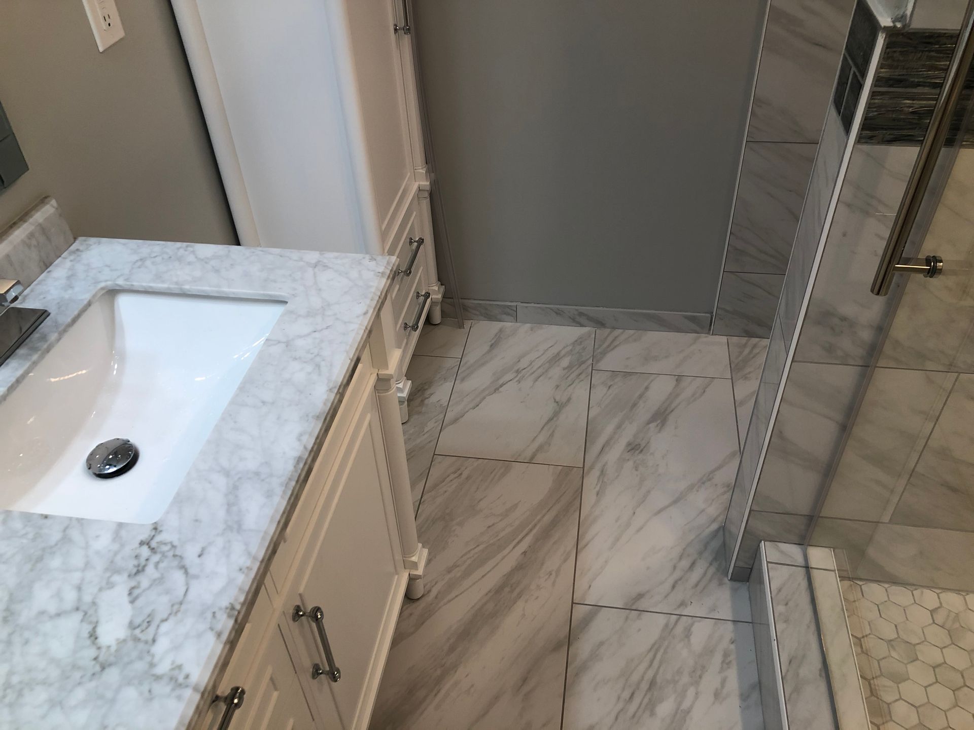 Modern bathroom with marble vanity, glass shower, and hex tile floor