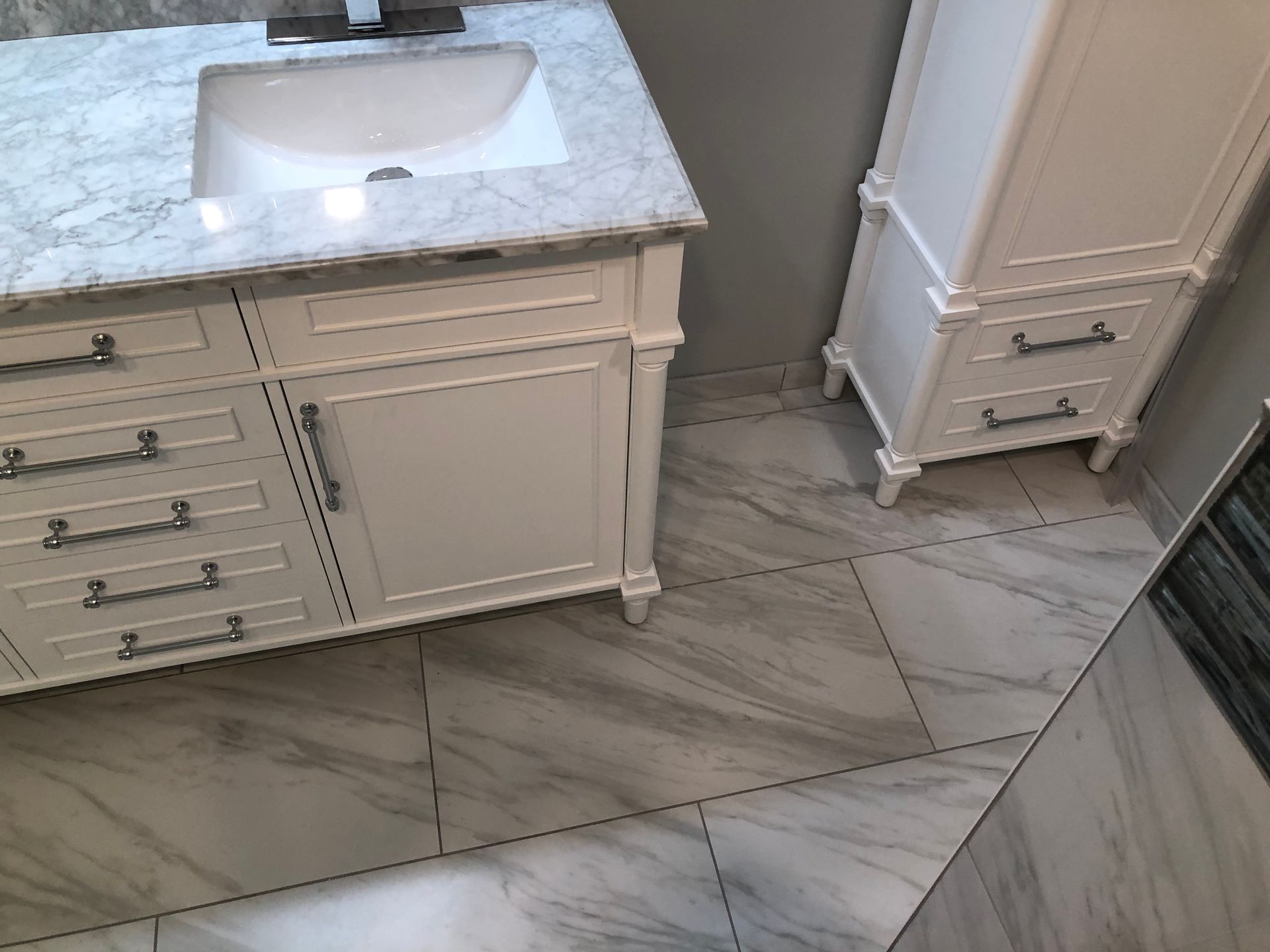 Bathroom vanity with white marble countertop, sink, drawers, and light gray floor tile.