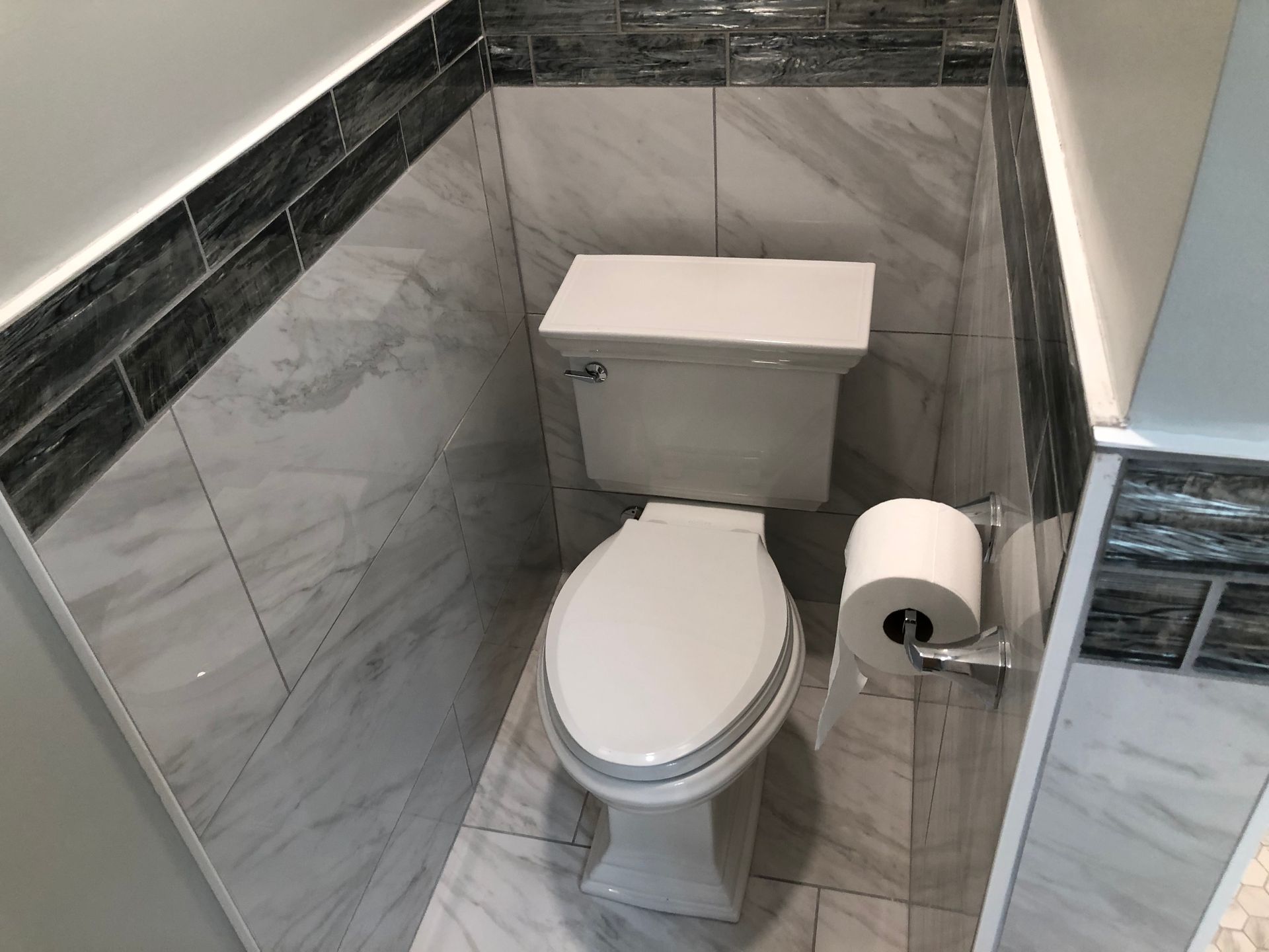 Small tiled bathroom with a white toilet and a toilet paper holder next to it.