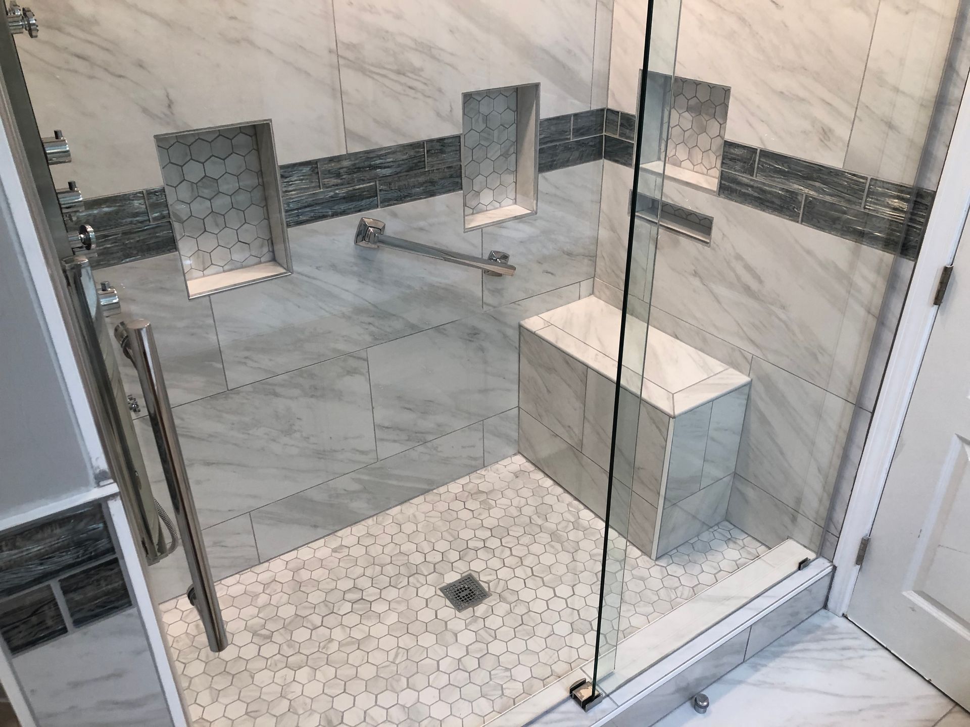 Glass shower with white marble tile, hex floor, built-in niches, and a small bench.