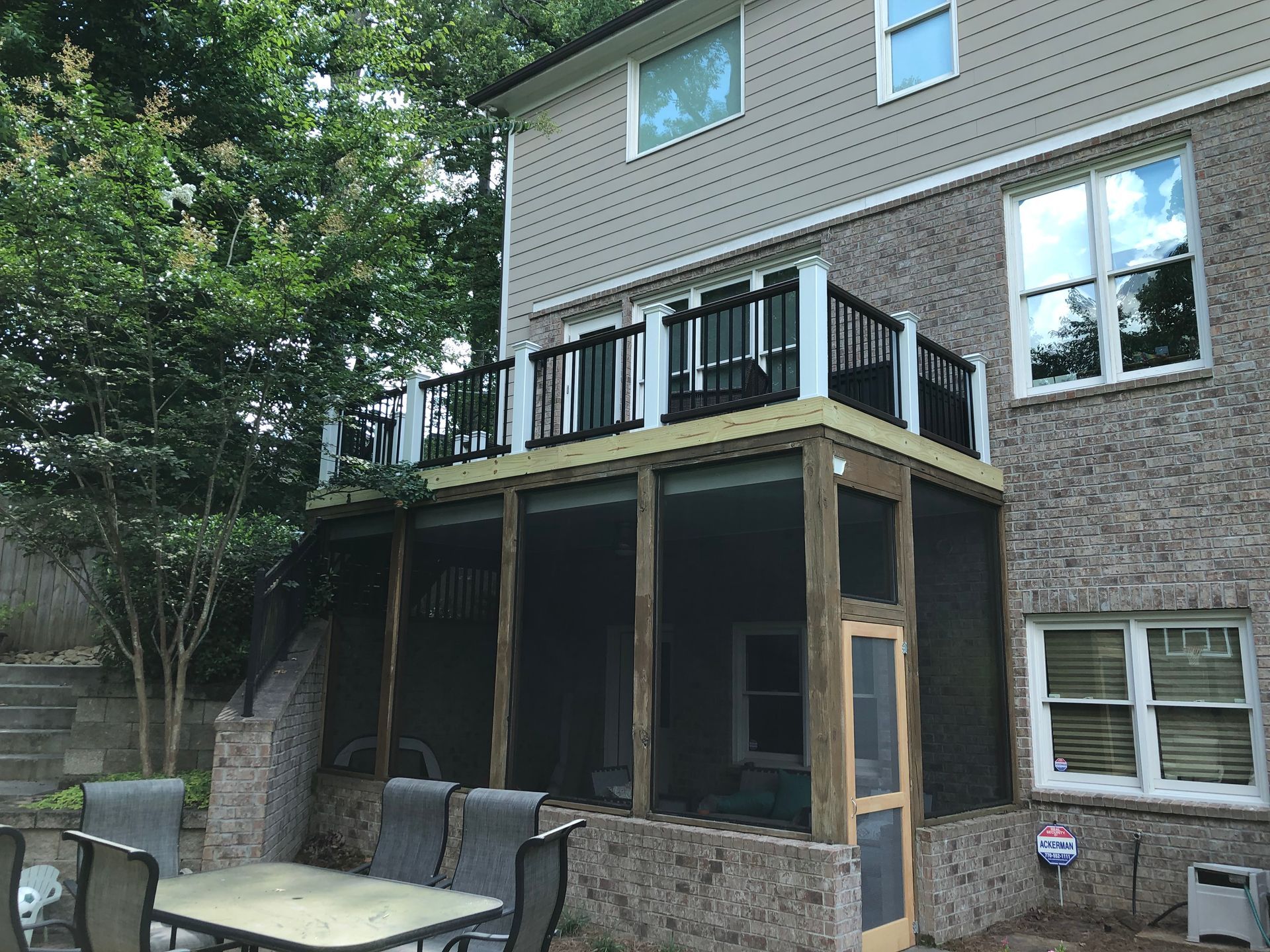 Backyard deck under construction on a brick house, with black railings and patio furniture below.