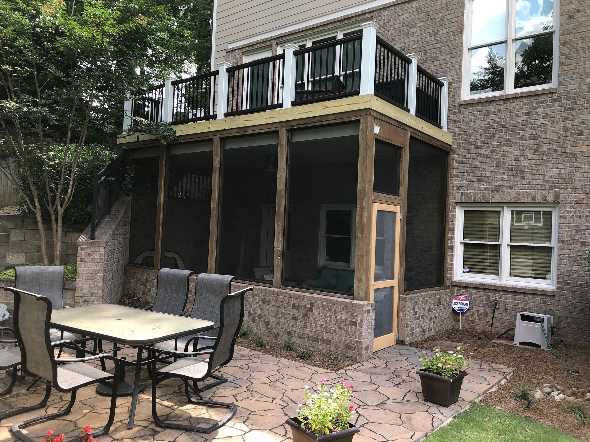 Back patio with stone pavers, outdoor dining table and chairs, and a covered deck under an upper balcony.