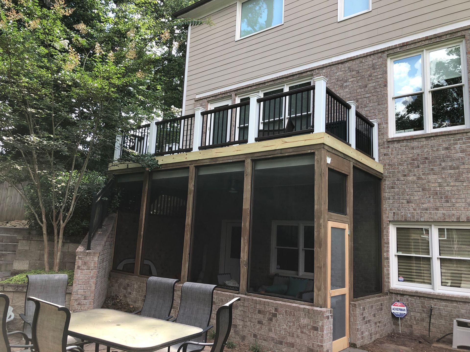 Backyard patio with screened porch, black-railed deck, and outdoor dining table beside a brick house