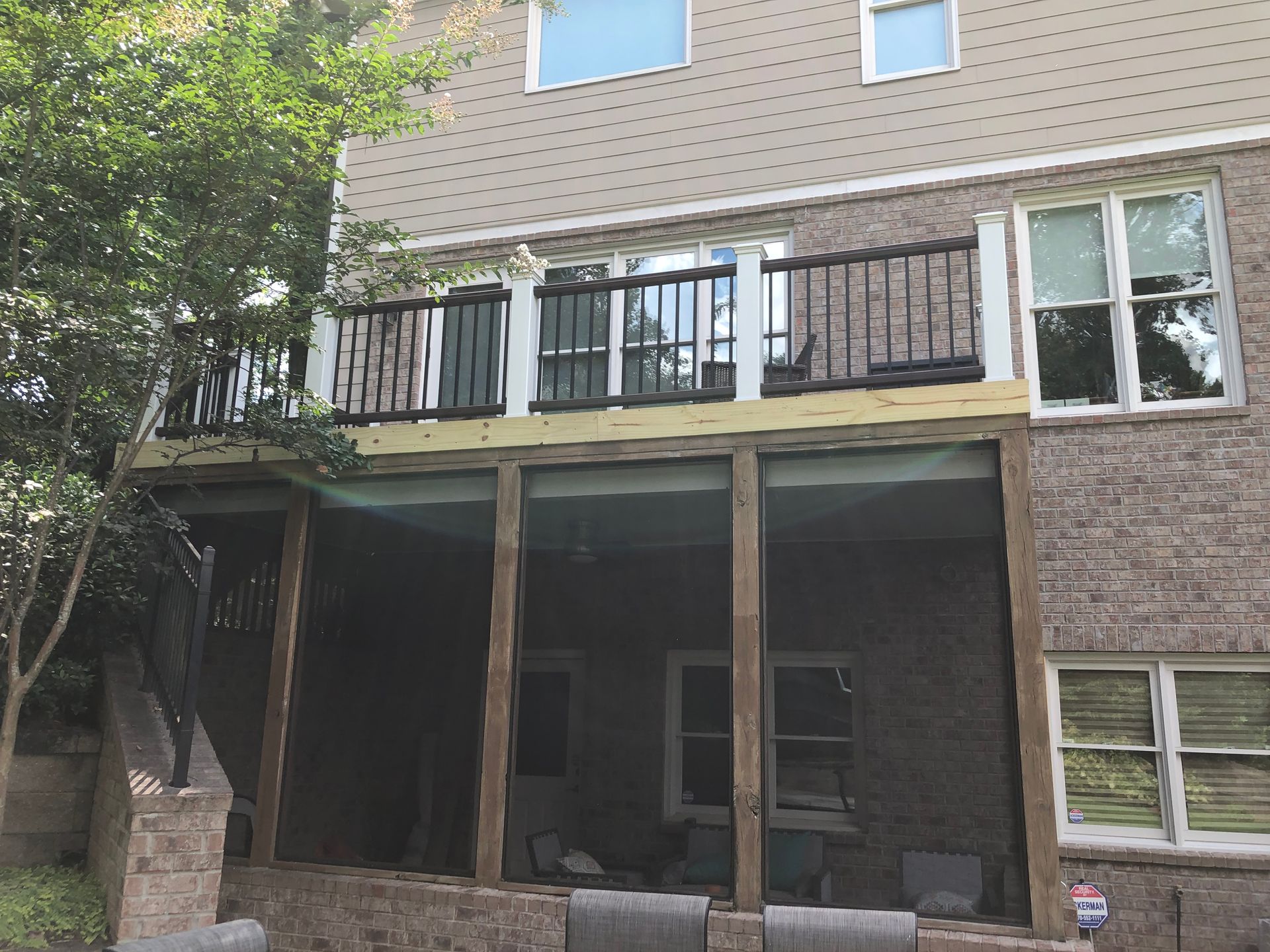 Brick house patio with screened porch, upper deck, and trees beside it