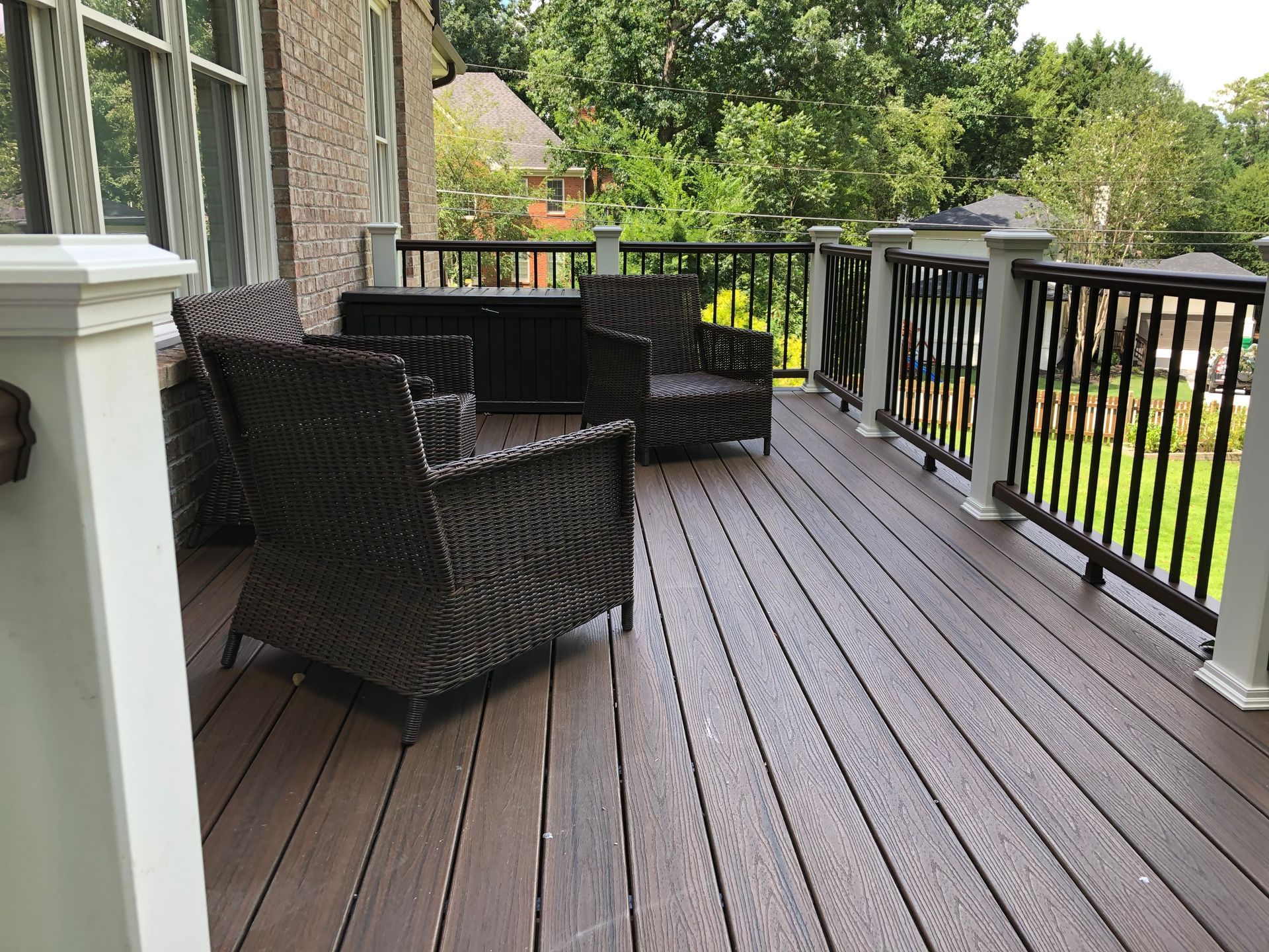 Covered wooden deck with black wicker chairs and railing overlooking a green yard.