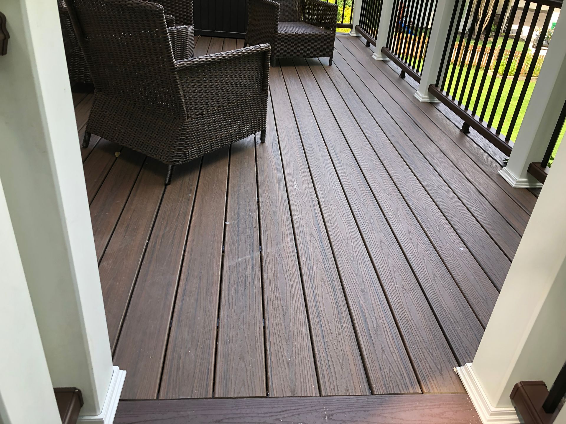 Wooden deck with dark wicker chairs and a railing overlooking a grassy yard