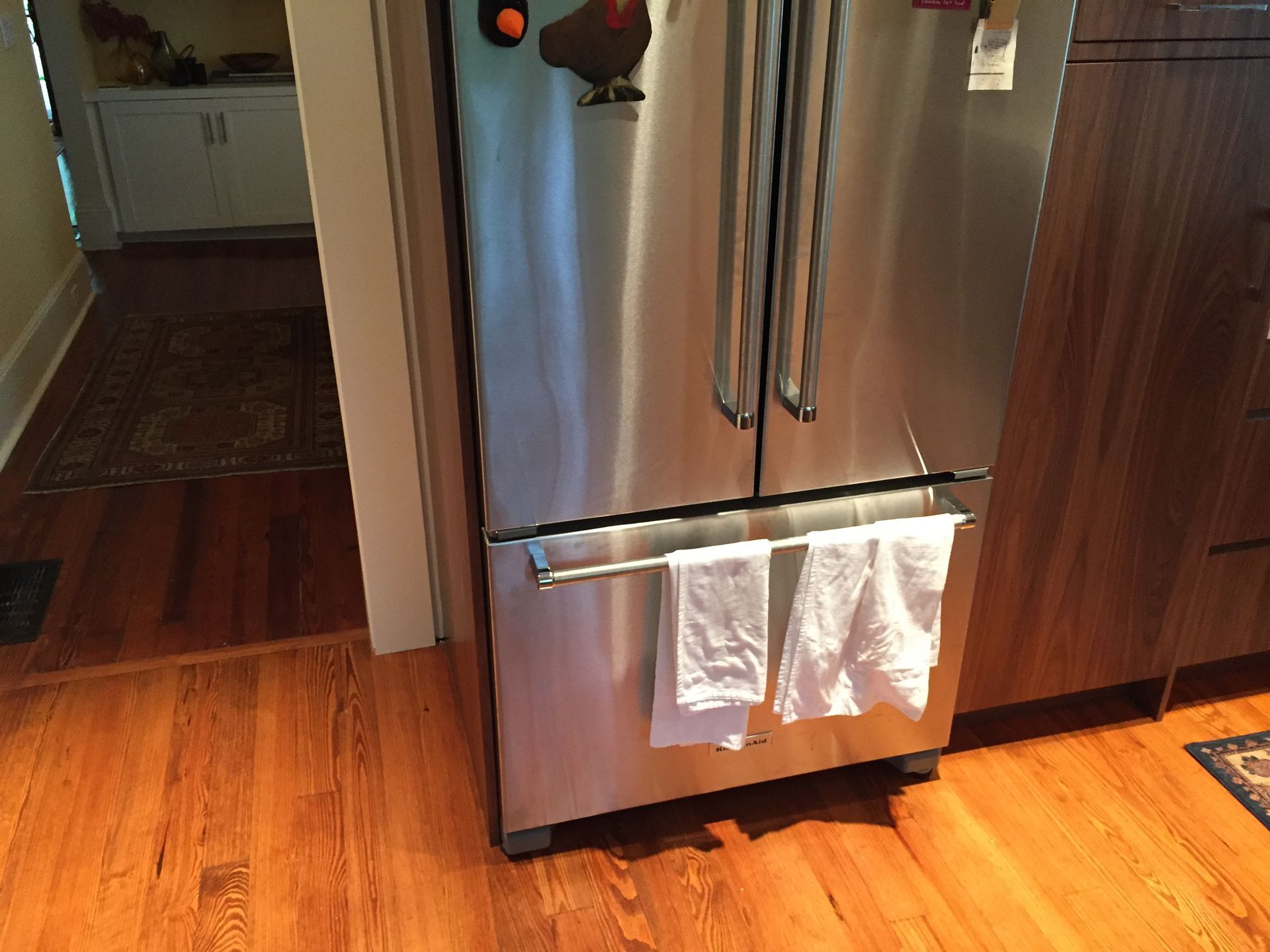 Stainless steel refrigerator in a kitchen with two white towels hanging on the handle.
