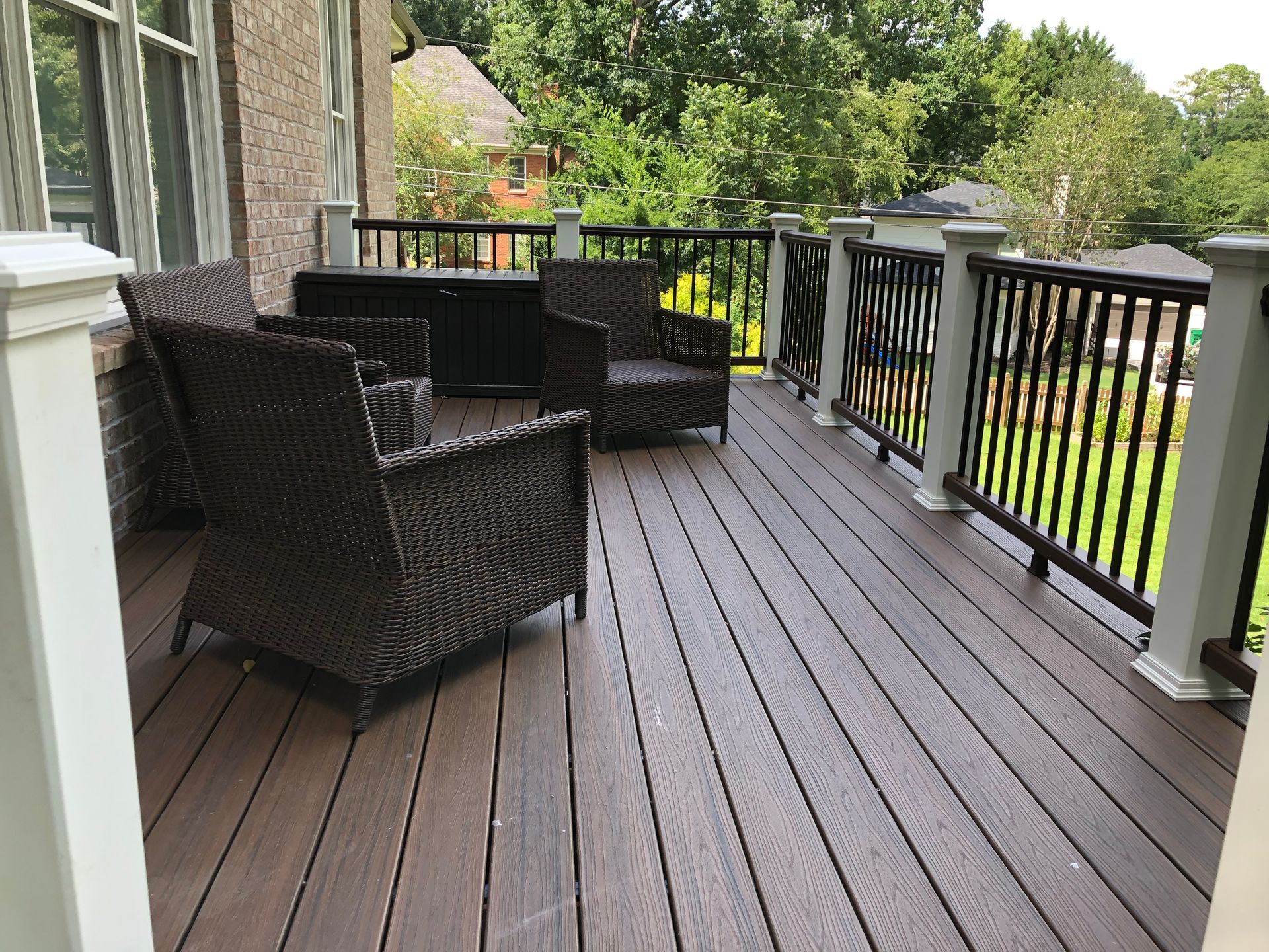Outdoor deck with dark wicker chairs, gray railings, and a wooded backyard view