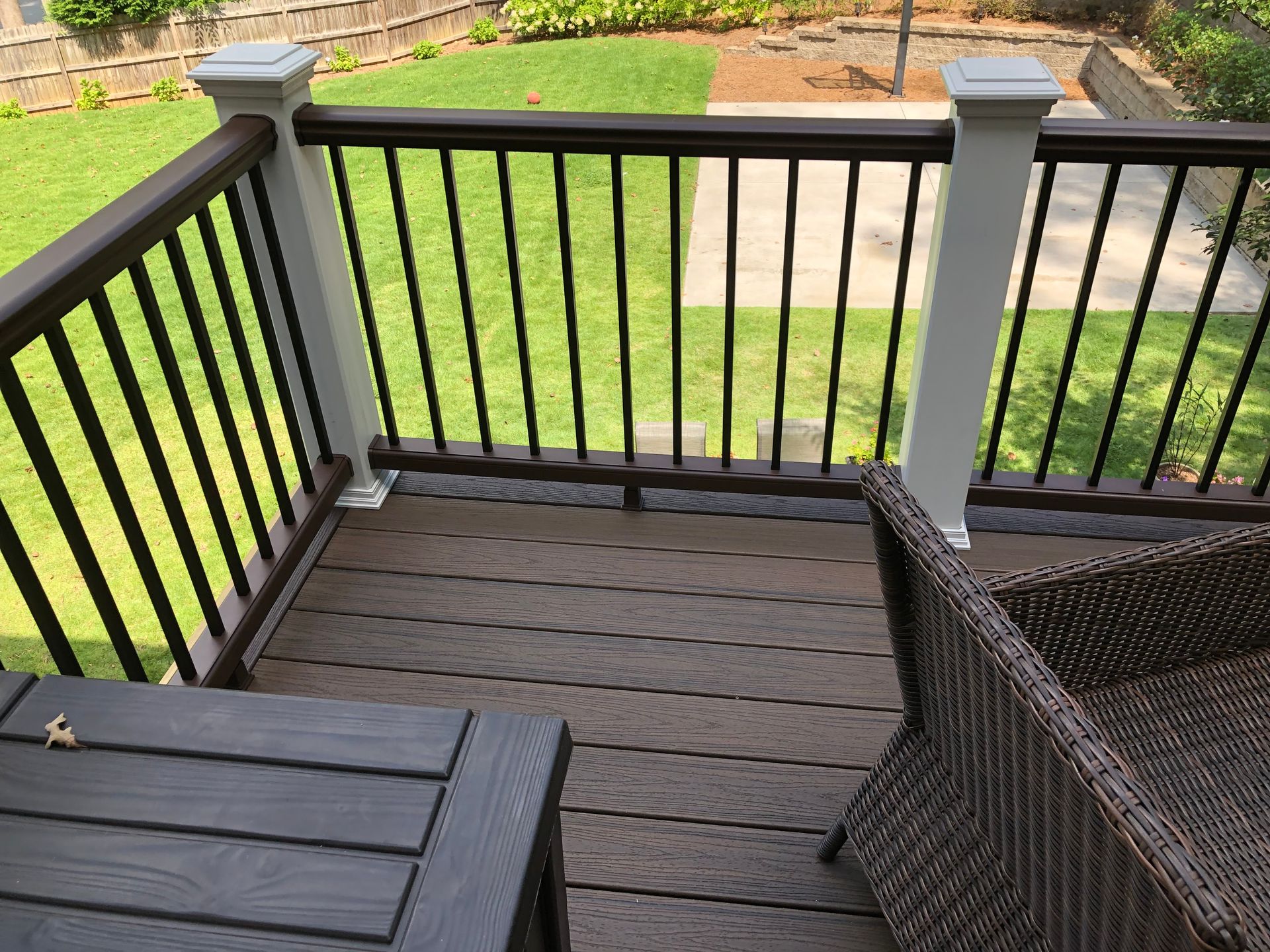 Back deck with black railing, brown floorboards, patio chair, and green lawn beyond
