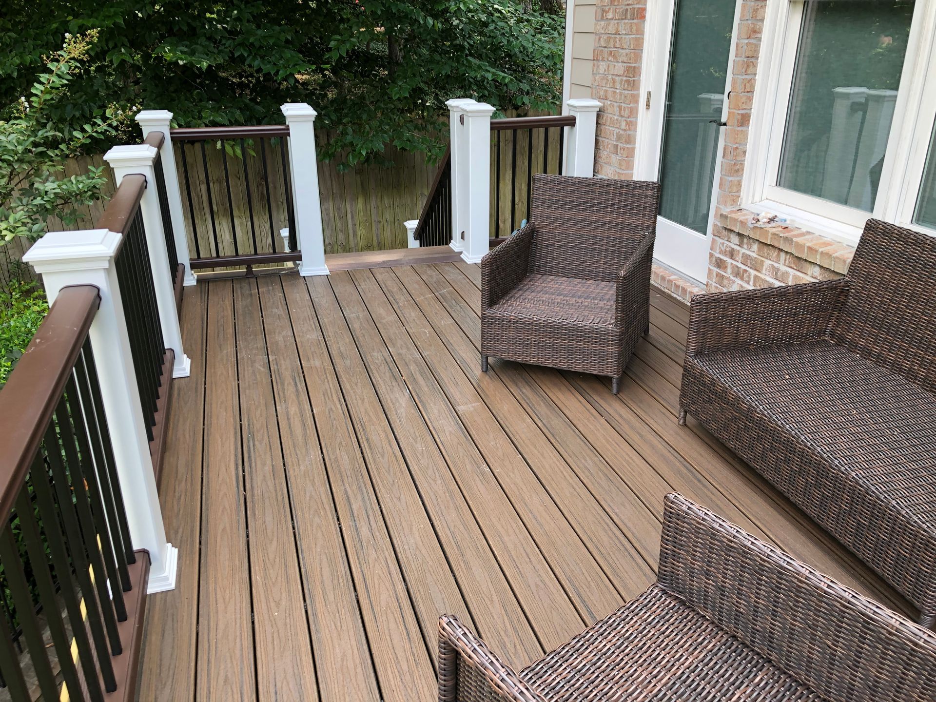 Wooden backyard deck with wicker chairs, railing, and potted plants beside a house.