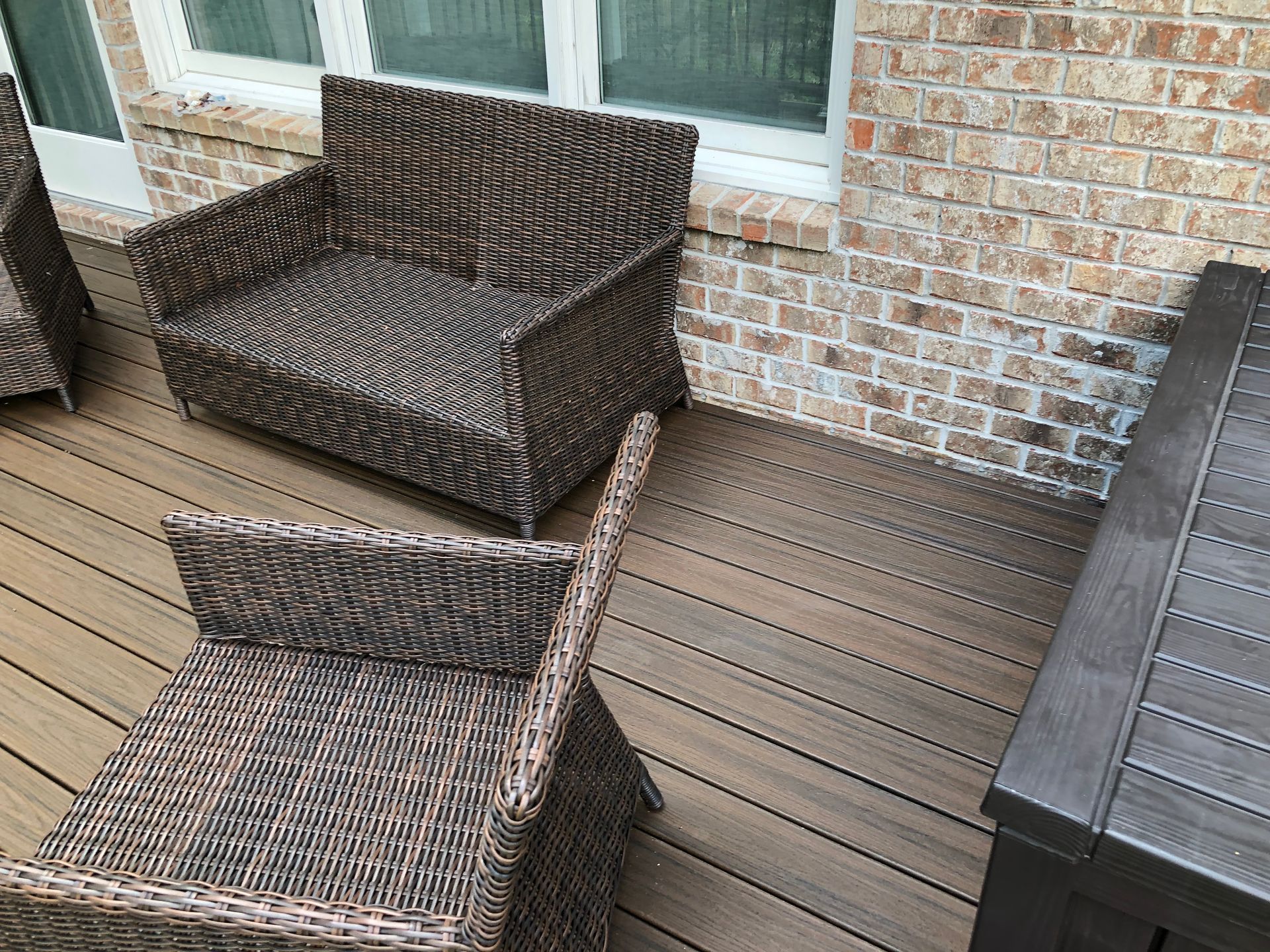 Wicker patio chairs and a table on a wooden deck beside a brick house