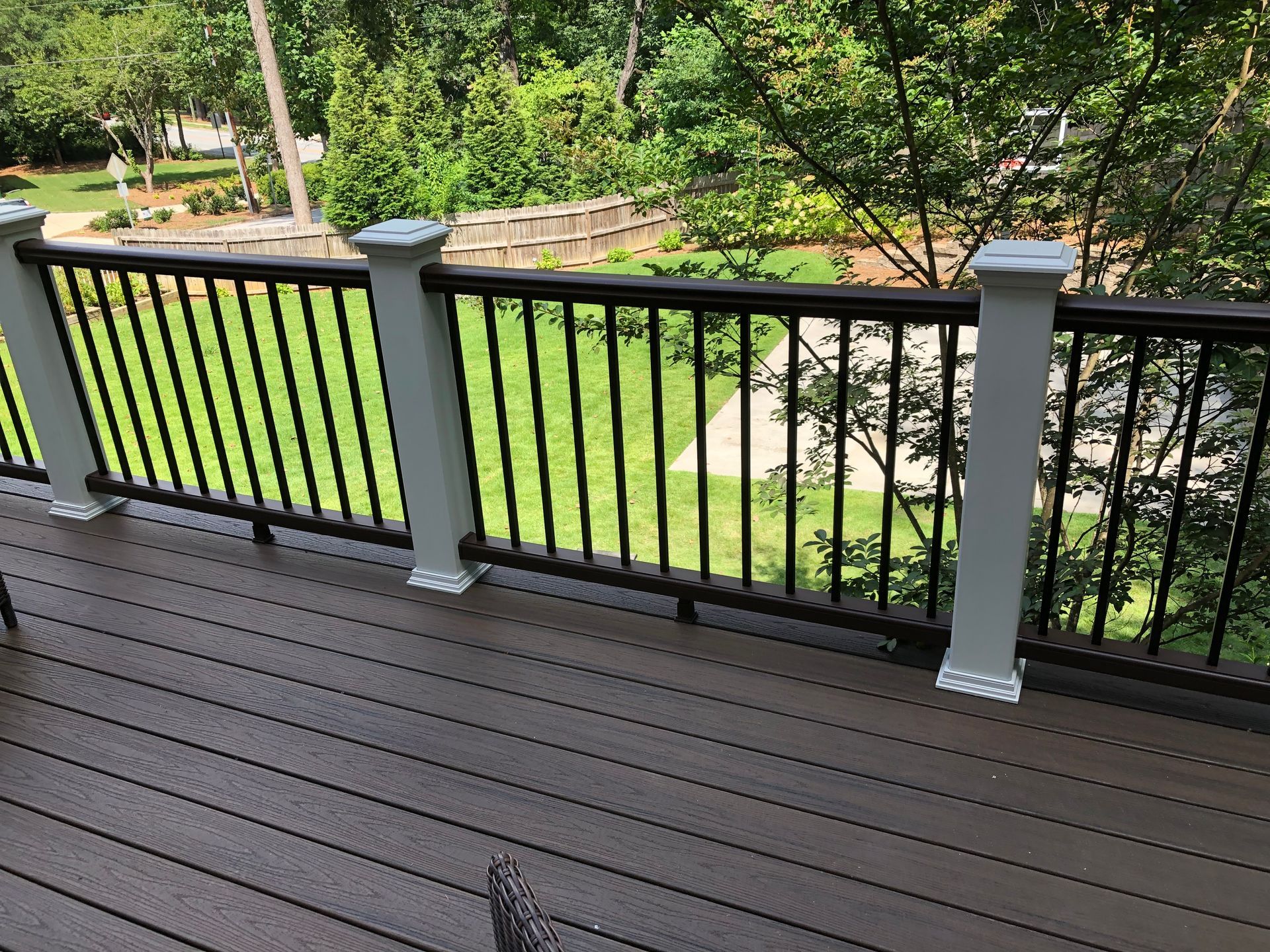 Wooden deck overlooking a green backyard with black railing and trees beyond