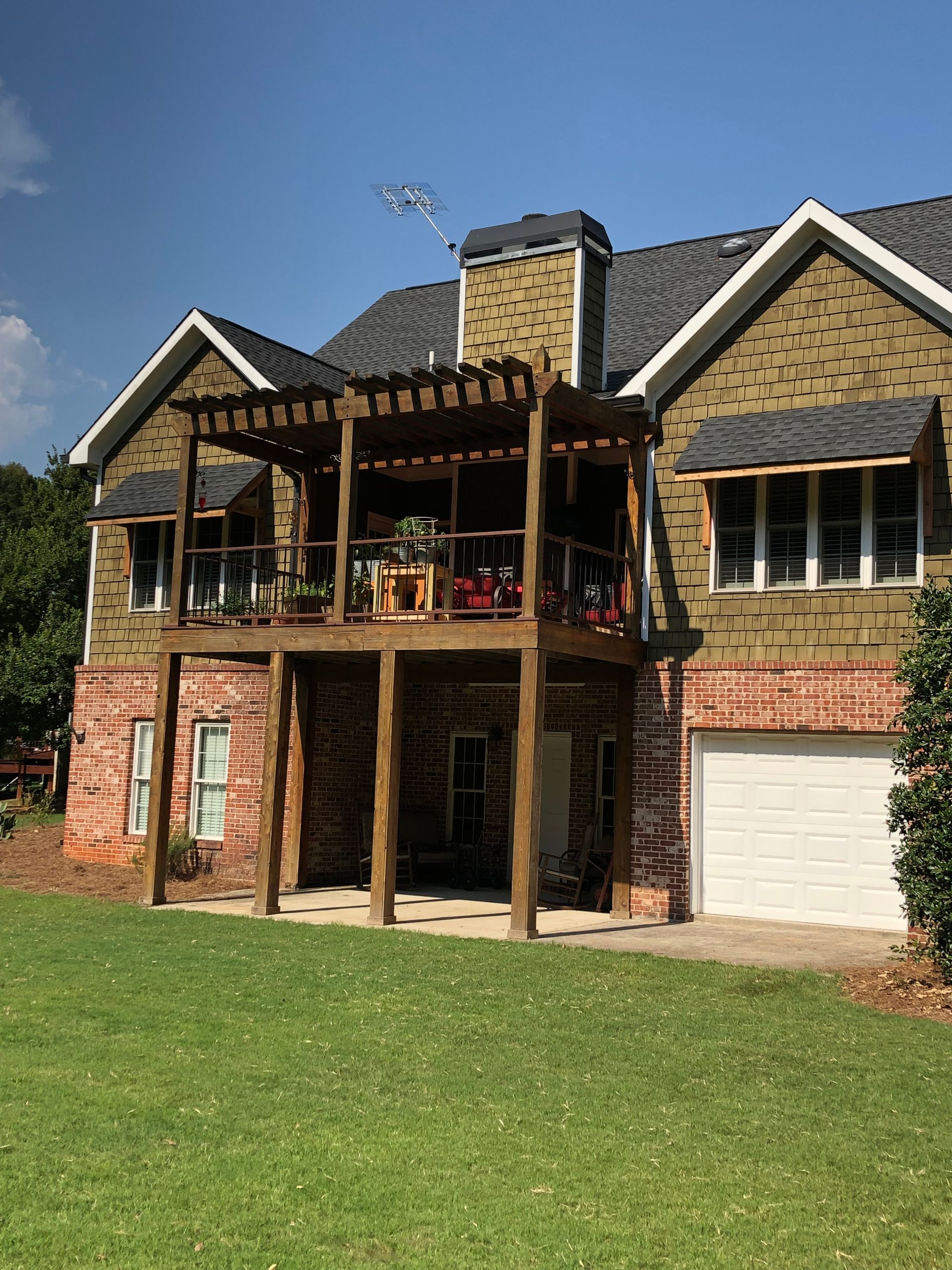 Two-story brick house with balcony, garage, and green lawn under a blue sky