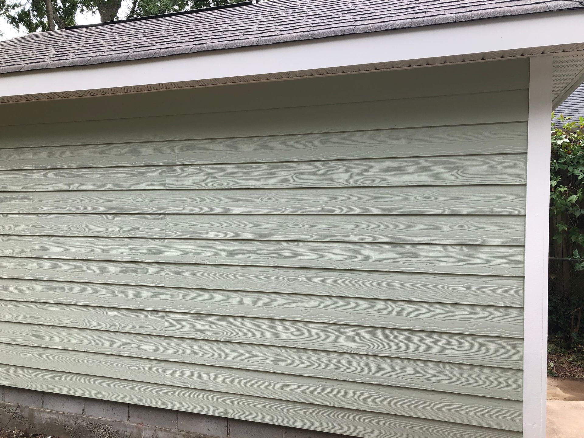 White house siding beneath a shingled roof, with a narrow window visible on the right