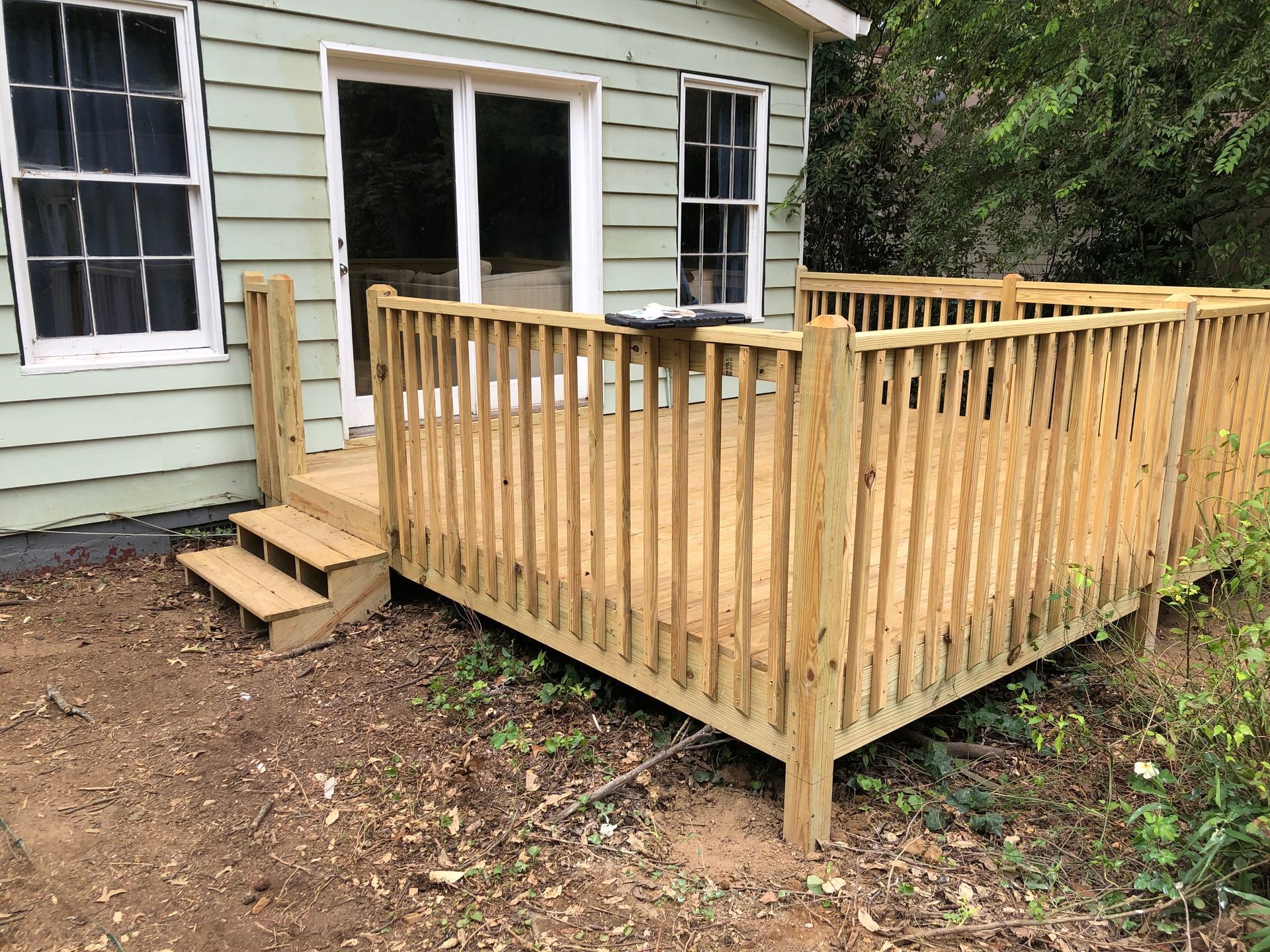 Wooden deck and ramp beside a light green house, with steps leading to the entrance.