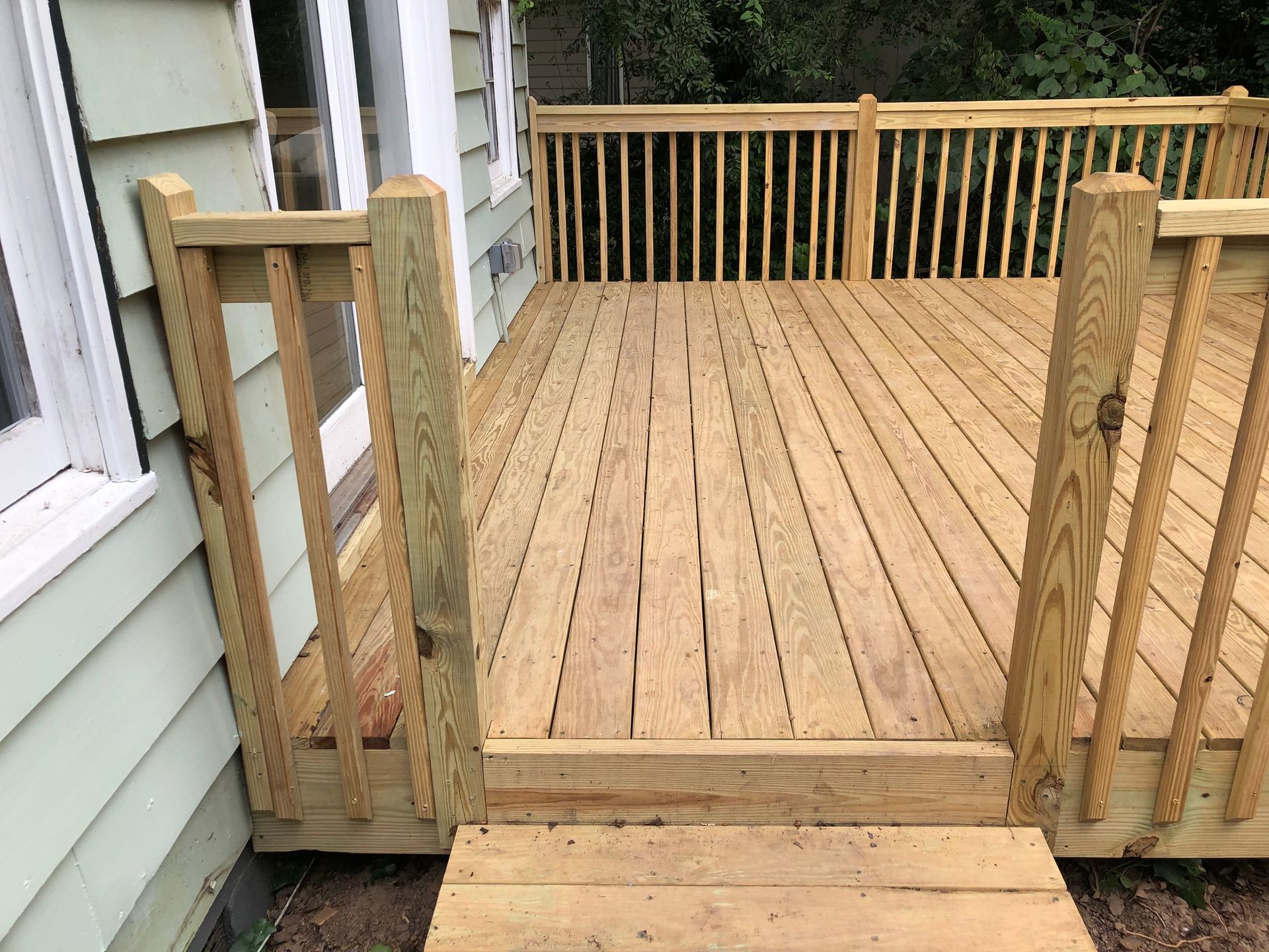 Wooden deck with steps and railing leading to a porch beside a house