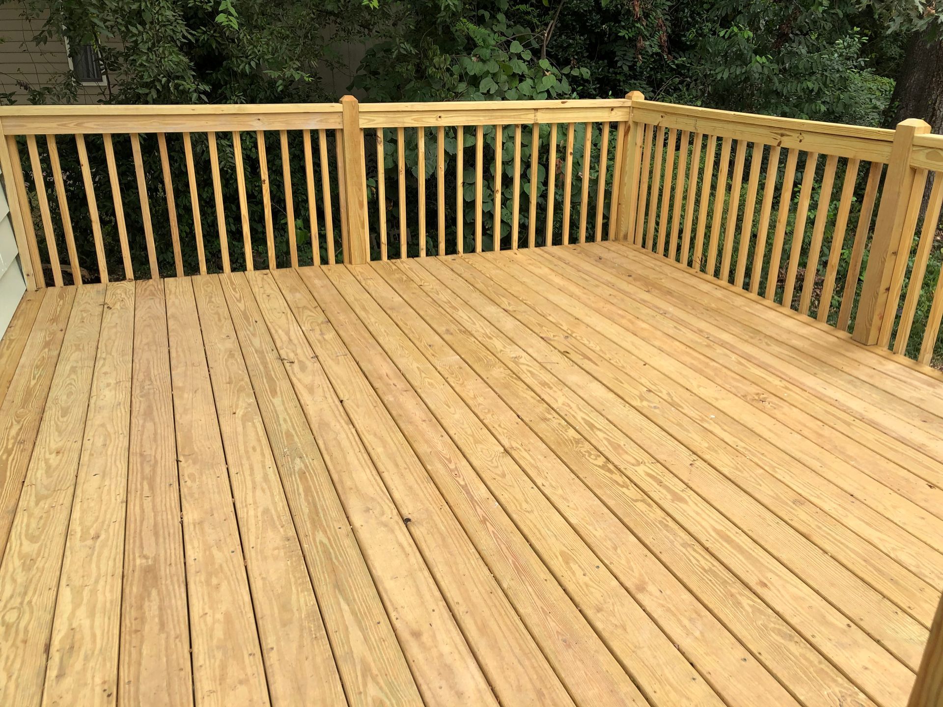 Wooden deck with light tan planks and railings, backed by green trees.