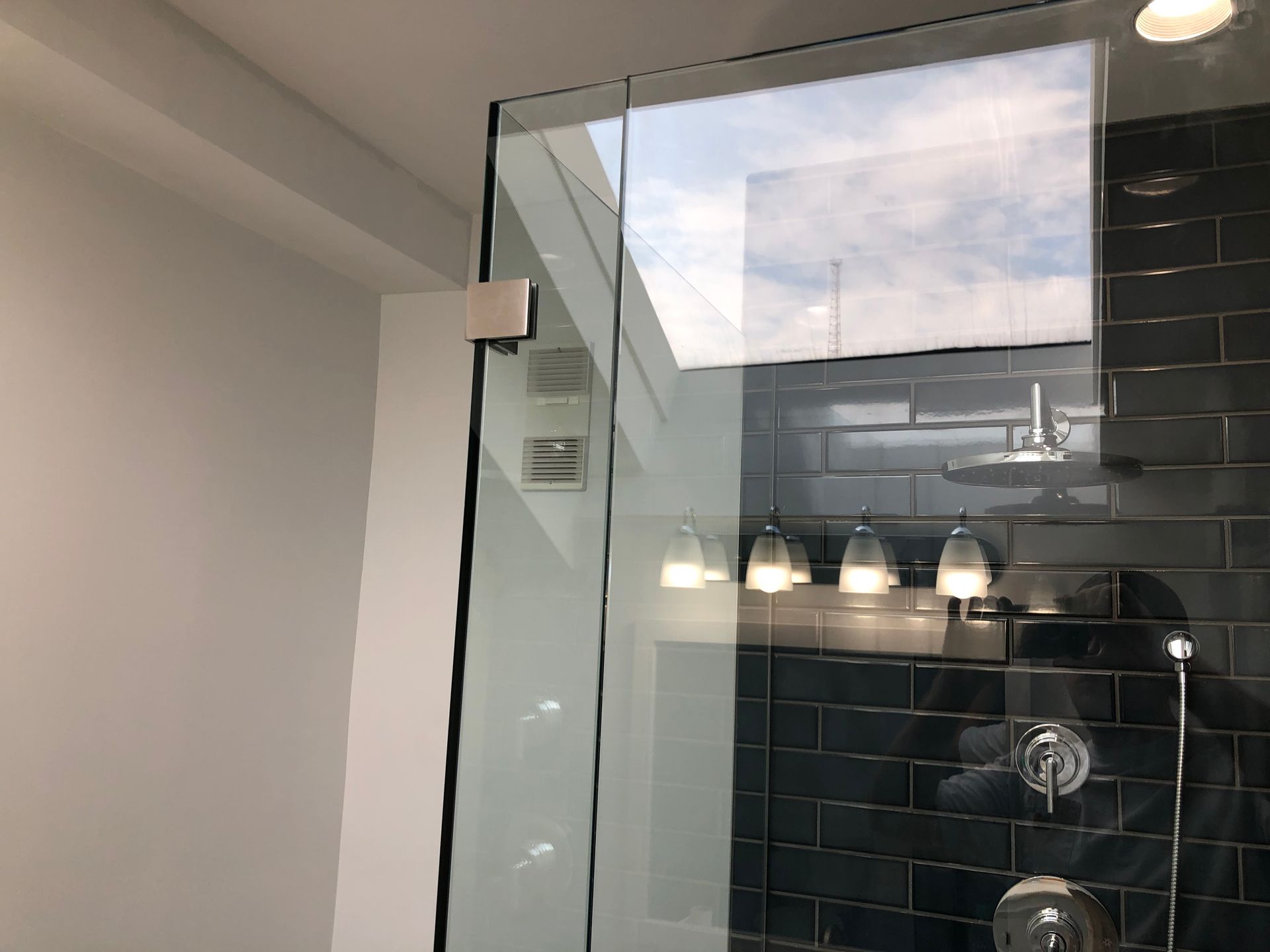 Glass shower enclosure with black tile and three wall lights in a modern bathroom