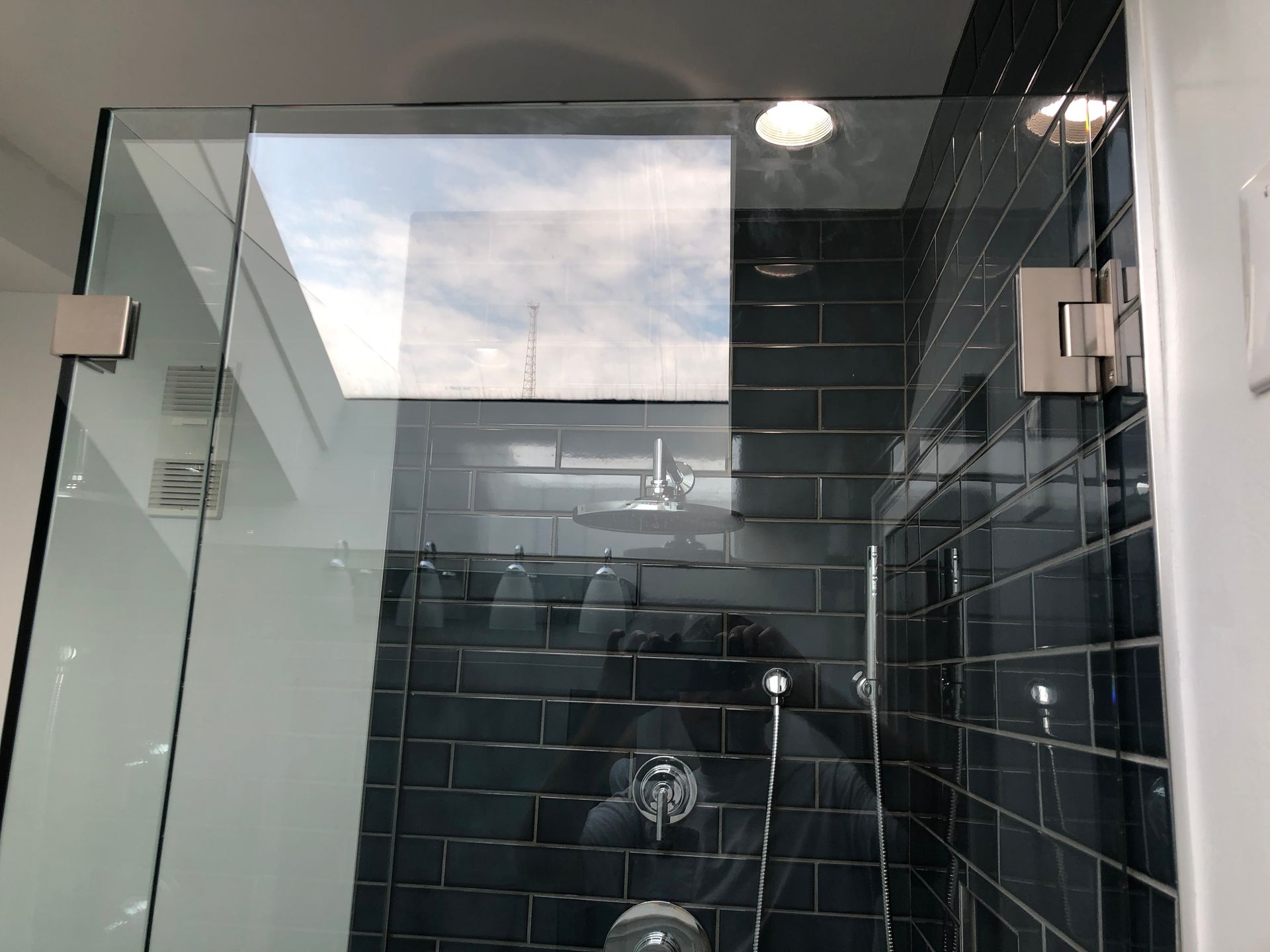 Modern glass shower with dark tile walls and a large window reflection above