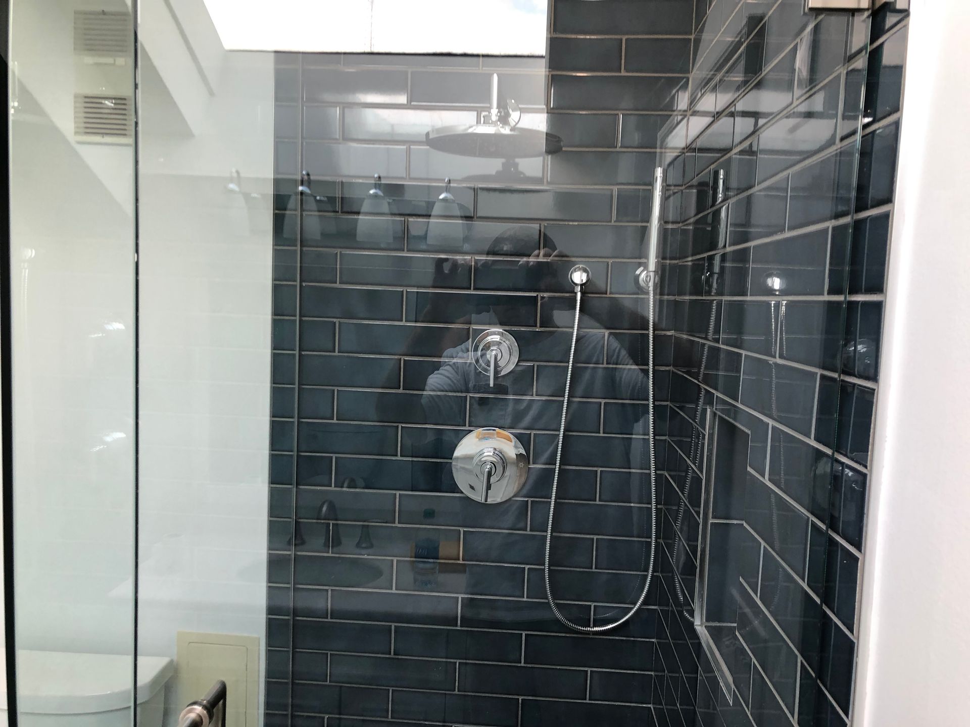 Modern bathroom shower with dark subway tiles and a chrome showerhead against a glass enclosure