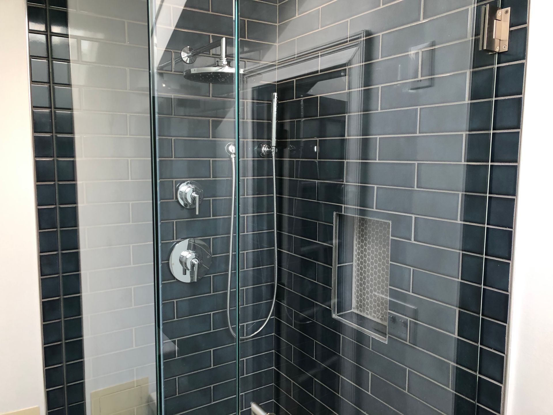 Modern shower with black tile, glass door, chrome controls, and built-in shelf niche