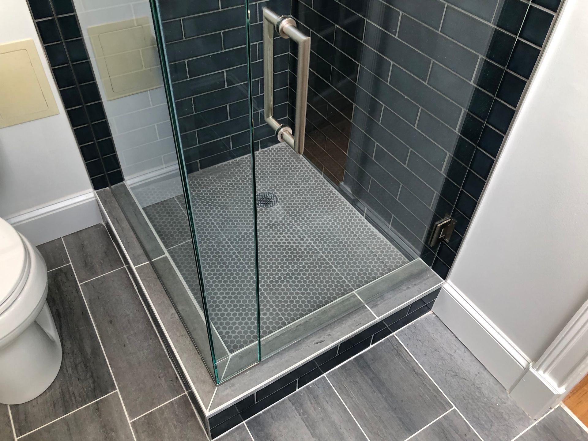 Glass shower enclosure with tiled walk-in shower and grab handle in a bathroom