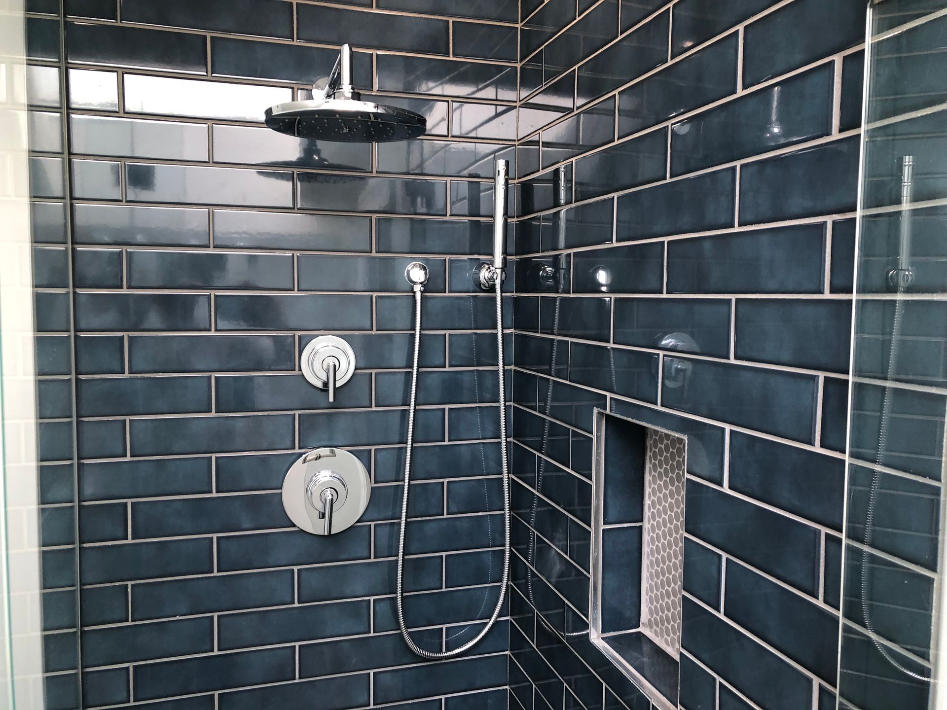 Modern bathroom shower with dark blue subway tile, chrome fixtures, and a recessed niche