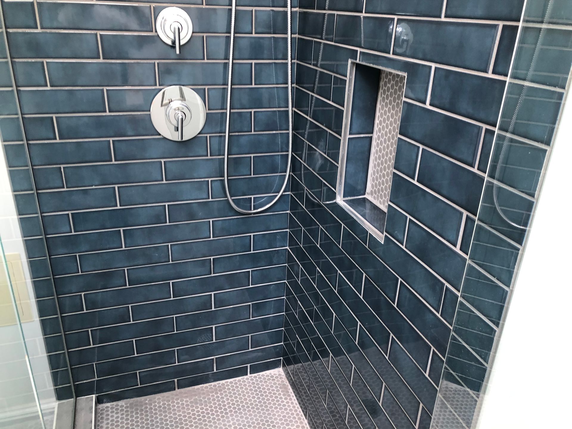 Dark blue tiled shower with chrome fixtures and a recessed shelf