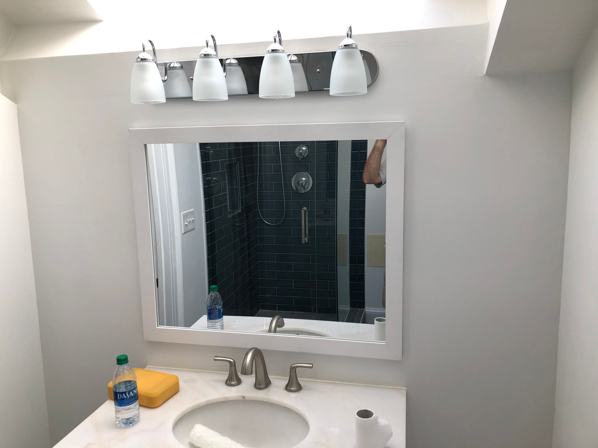 Bathroom vanity with mirror, four lights, sink, soap, and a bottle on the counter.
