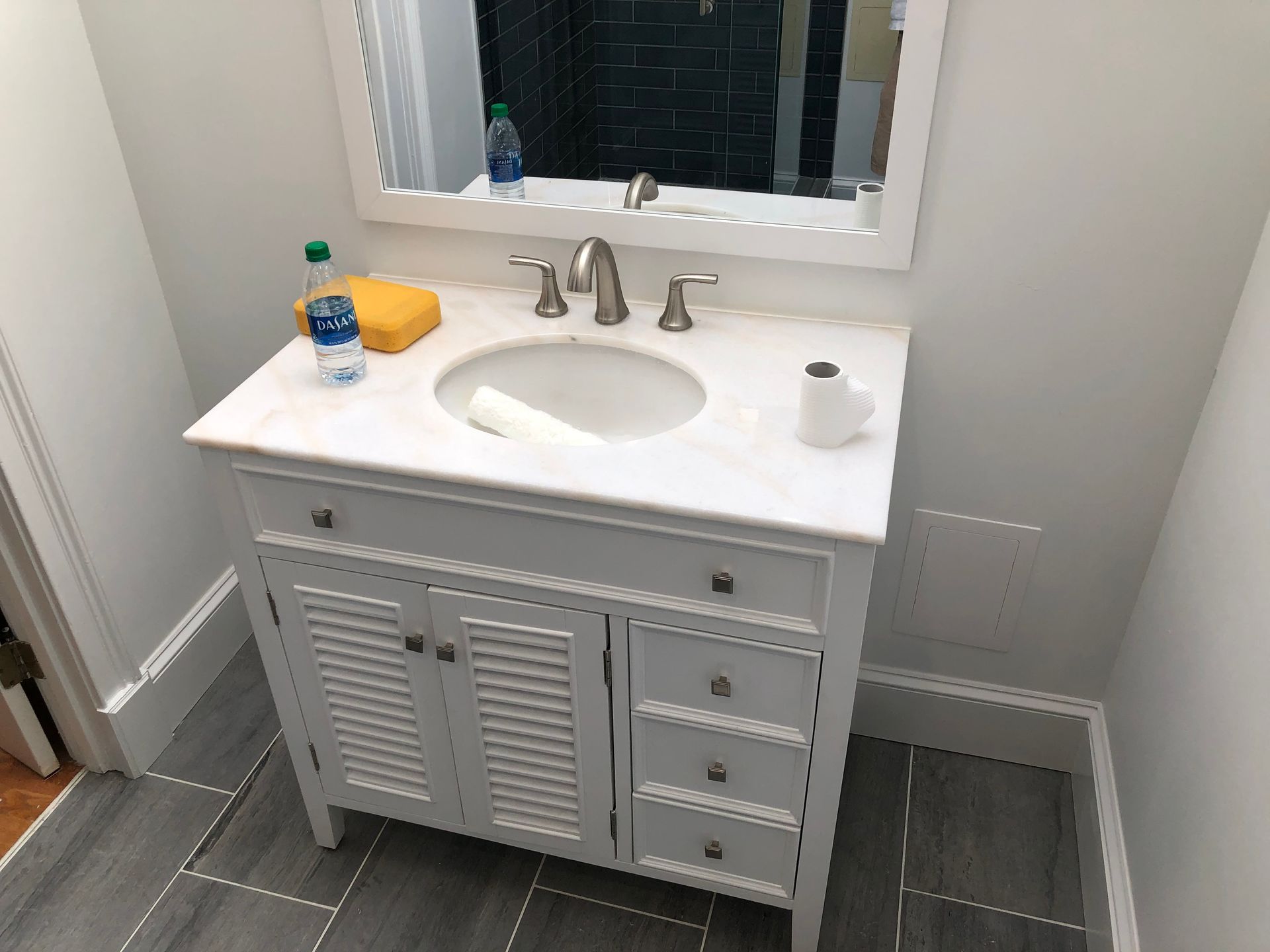White bathroom vanity with sink, mirror, soap, and tissue roll in a small tiled room