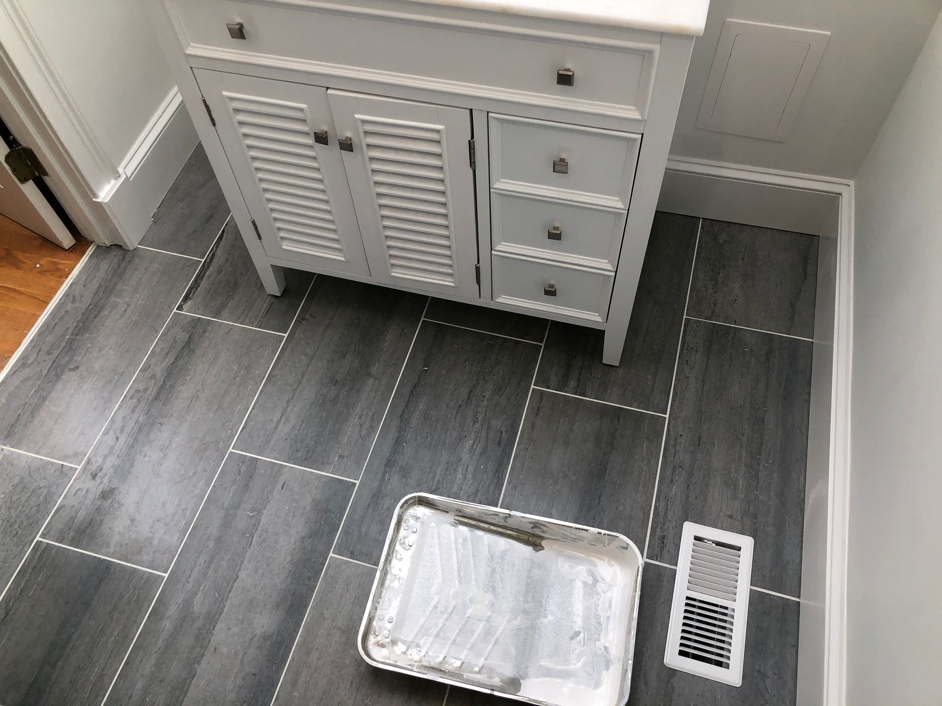 Gray bathroom floor with a vent, plastic tray, and vanity cabinet against the wall