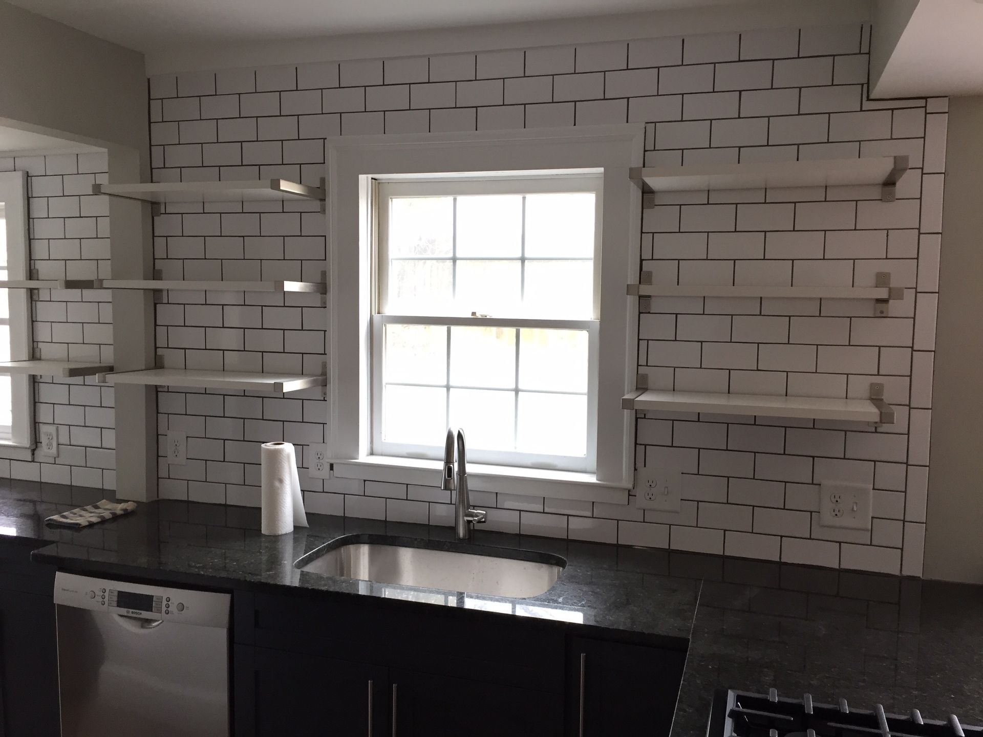 Modern kitchen with white tiled backsplash, black countertop, sink, and window above the sink