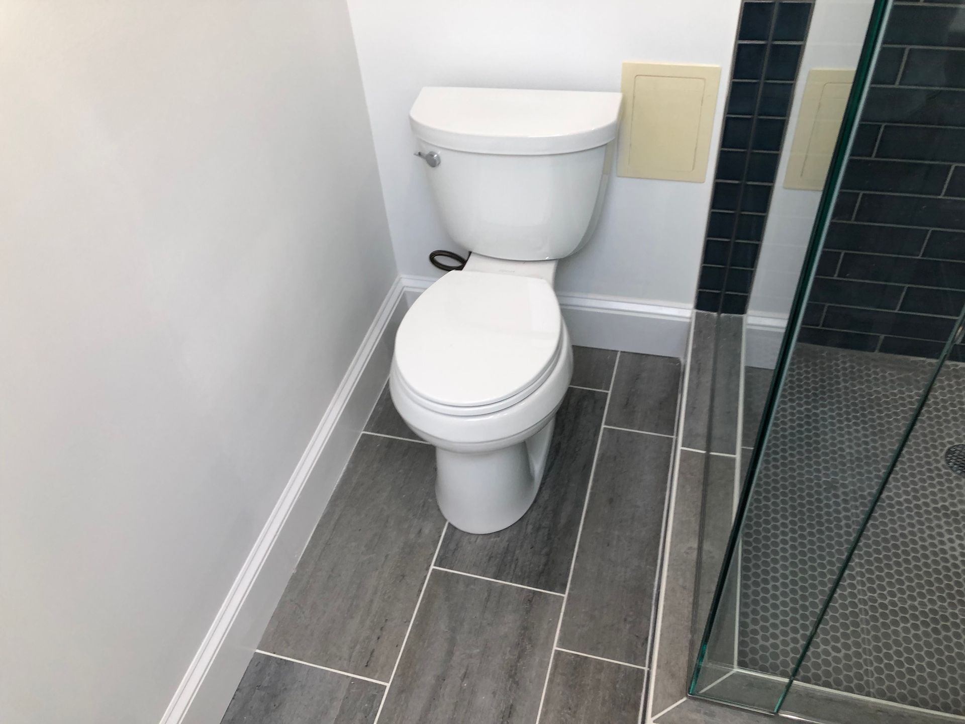 Small bathroom with a white toilet, gray tile floor, and glass shower enclosure.