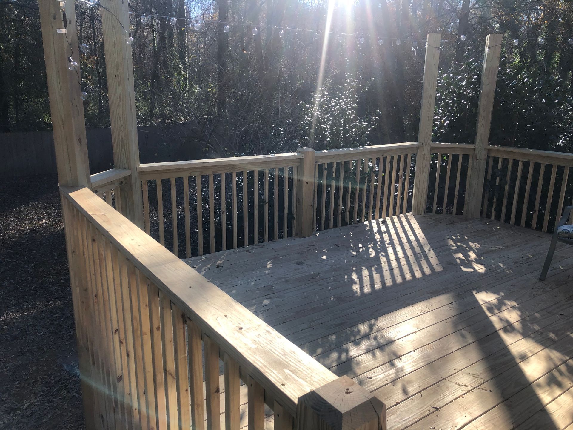 Sunlit wooden deck with railings and dappled shadows in a wooded area