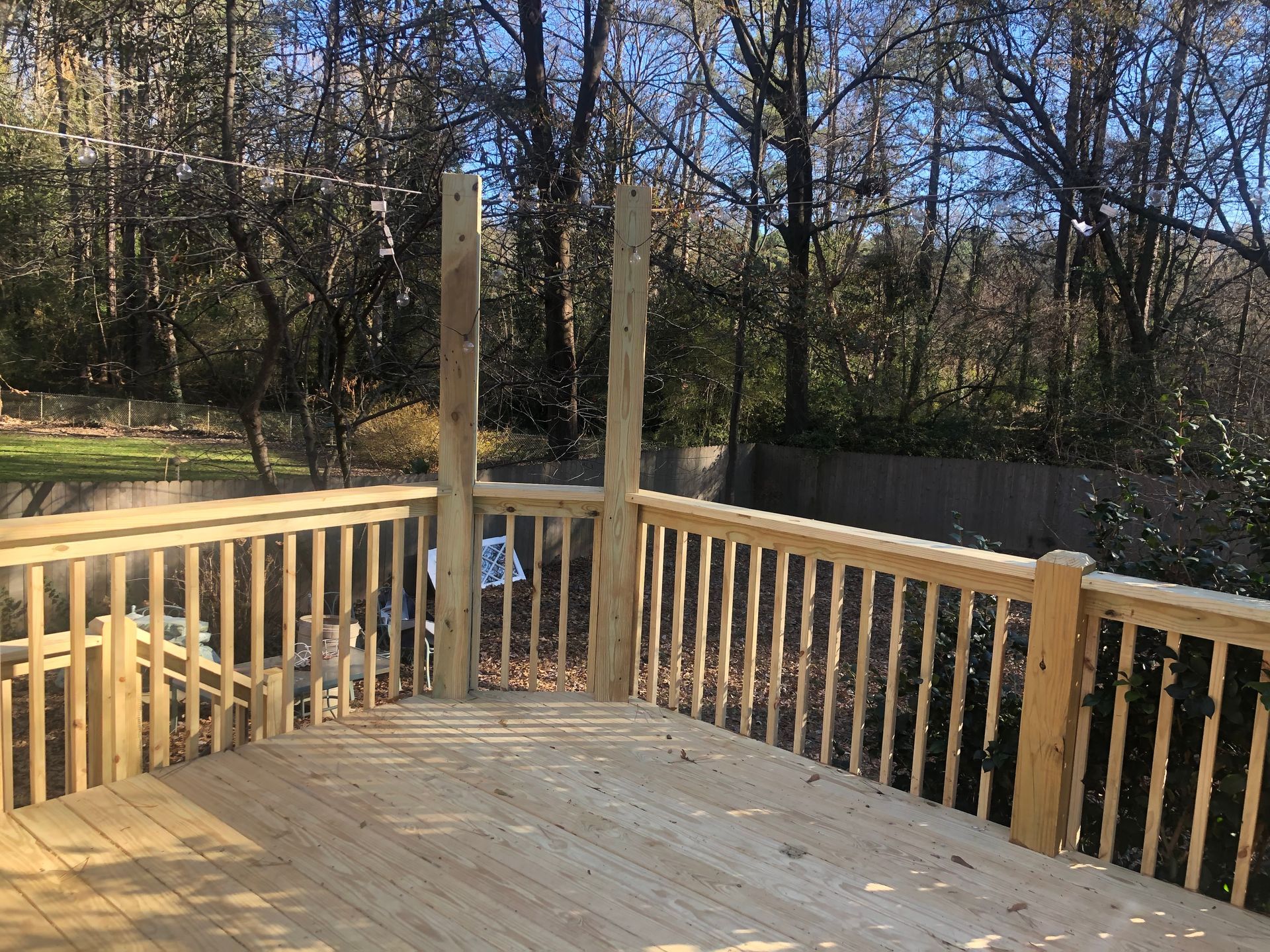 Wooden deck with railings and two posts overlooking a wooded backyard