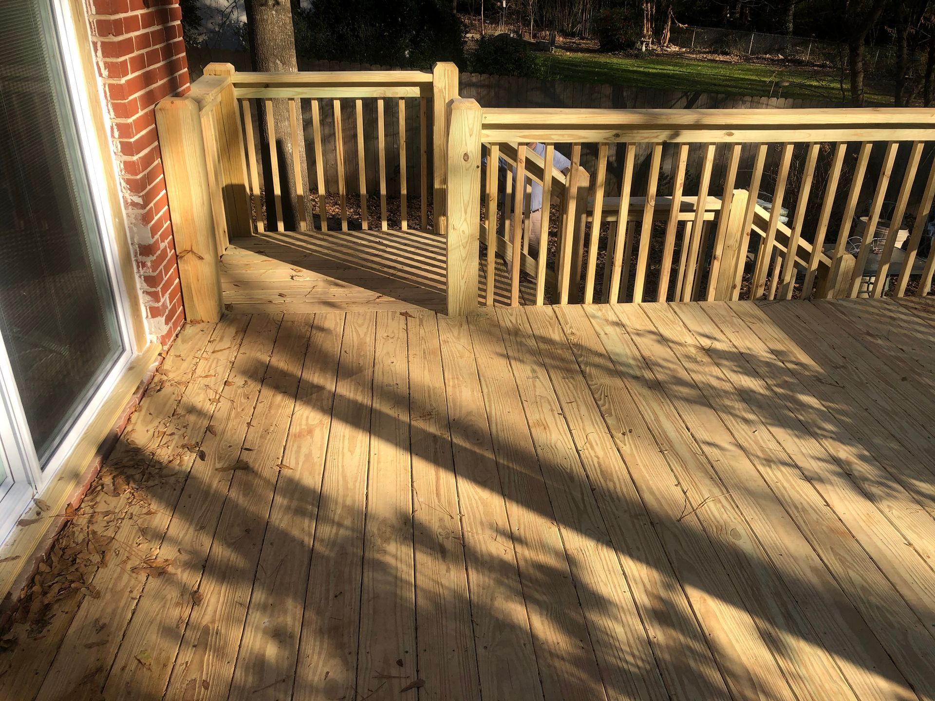 Wooden deck with railing beside a brick house, lit by long afternoon shadows.