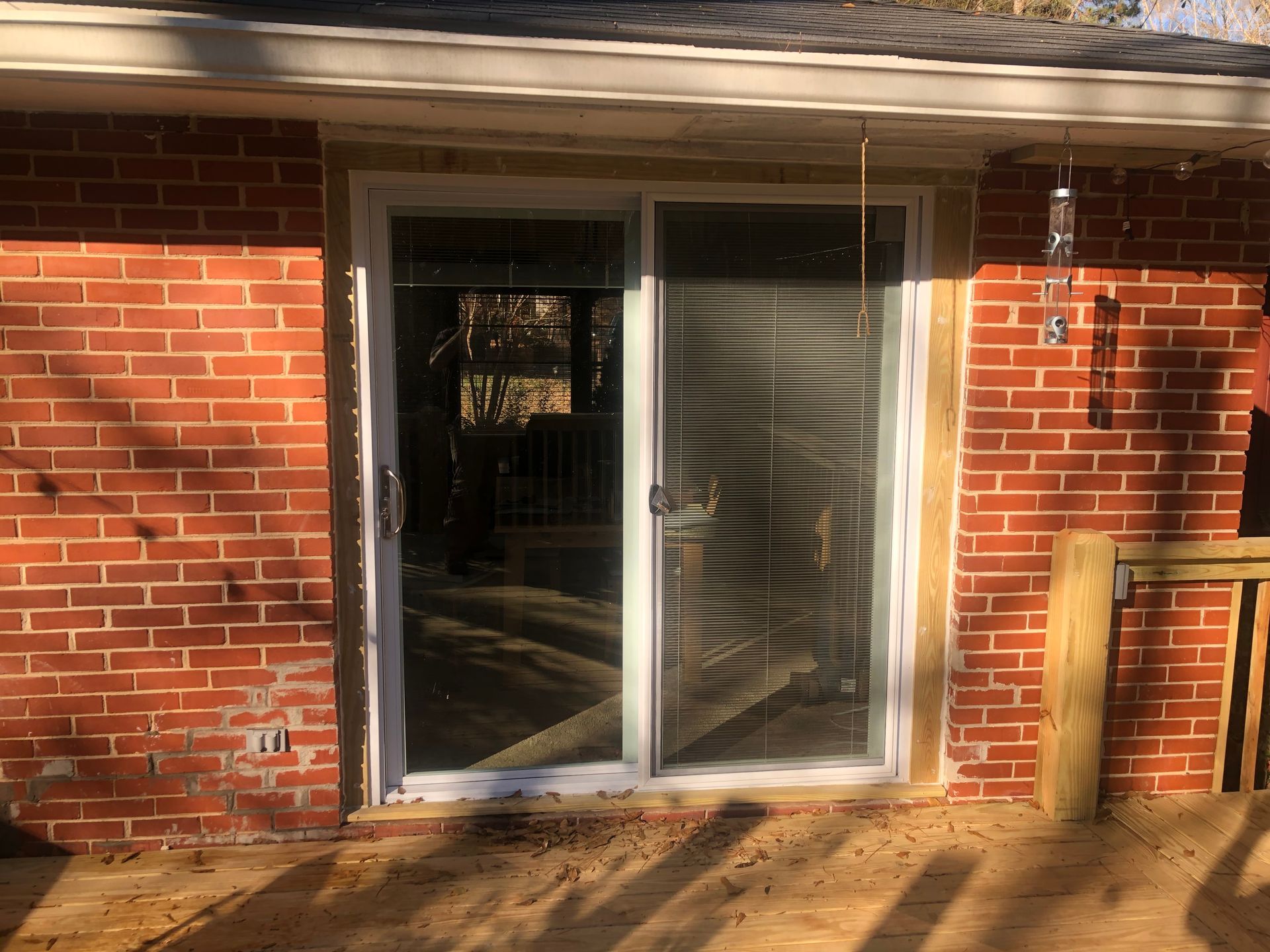 Sliding glass door in a red brick wall with sunlight and a wooden deck in front