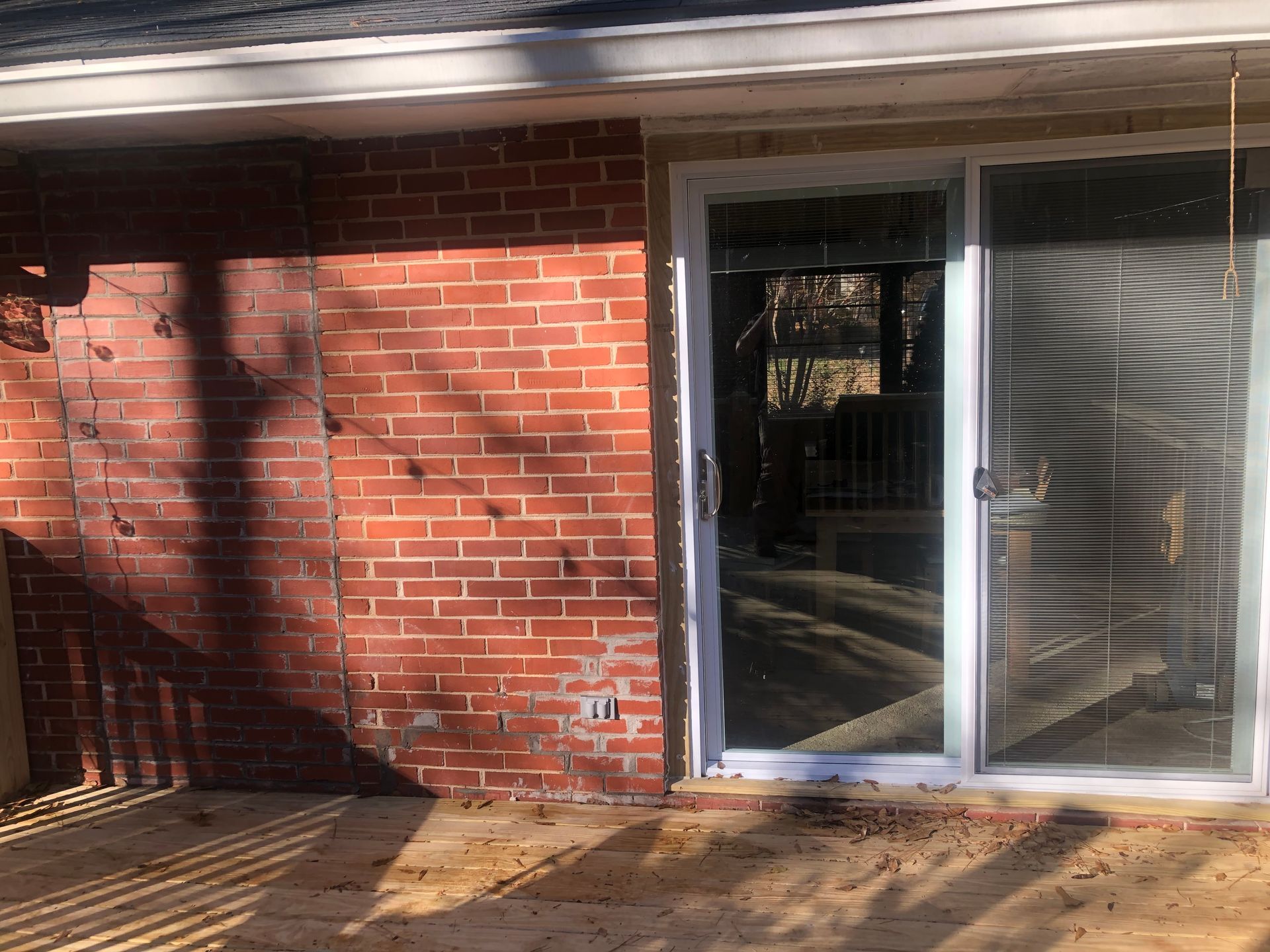 Brick exterior wall beside a sliding glass door and wooden deck in sunlight