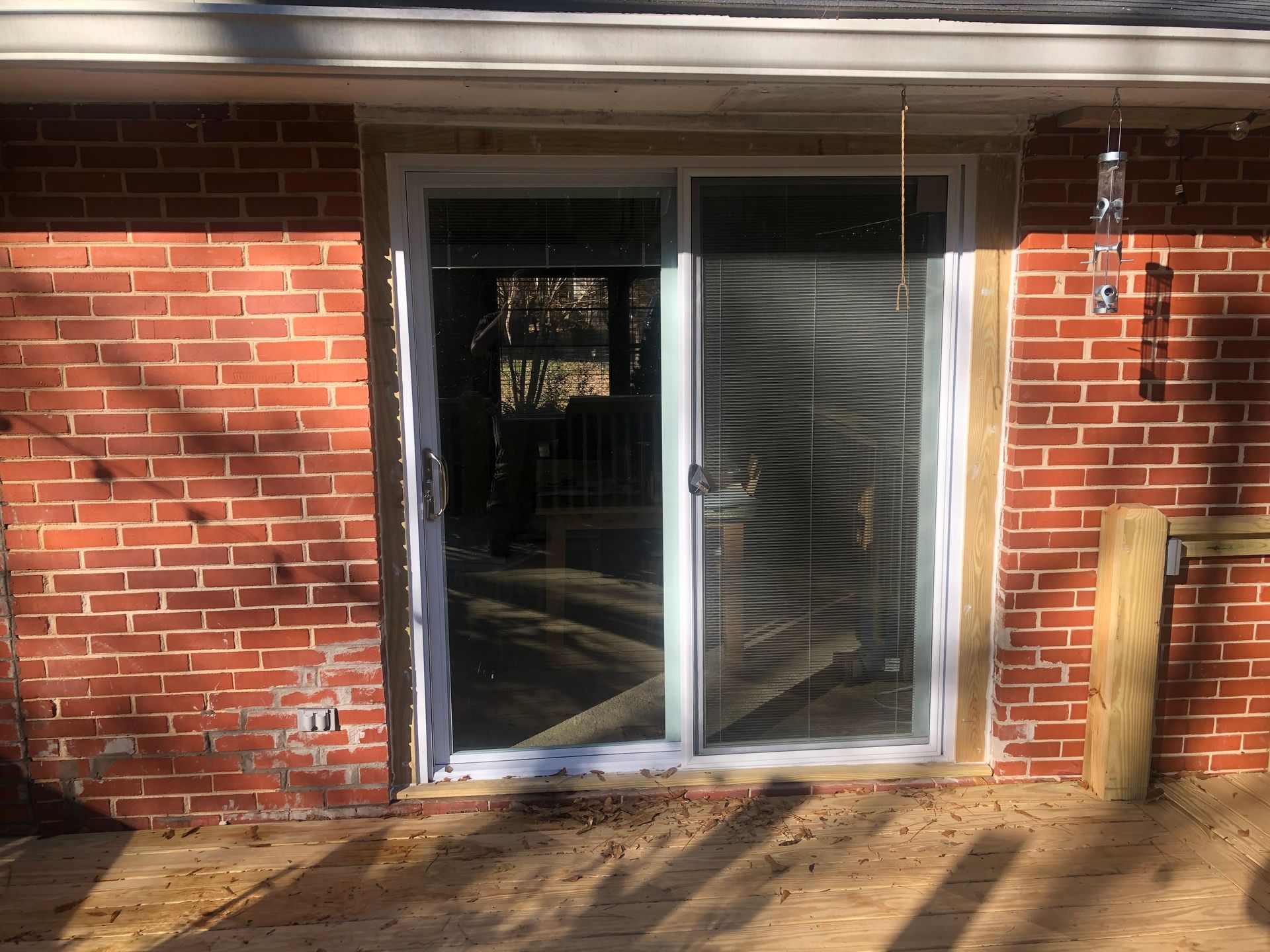 Brick patio with a sliding glass door and white blinds, with sunlight casting shadows.