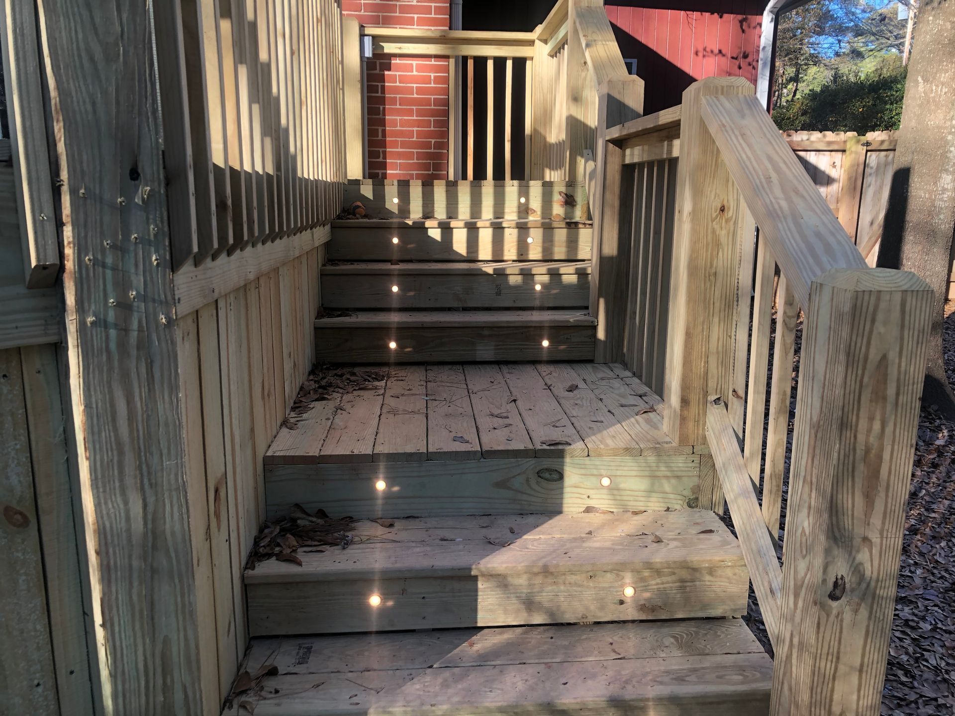 Wooden outdoor stairway and ramp leading to a red house porch in sunlight