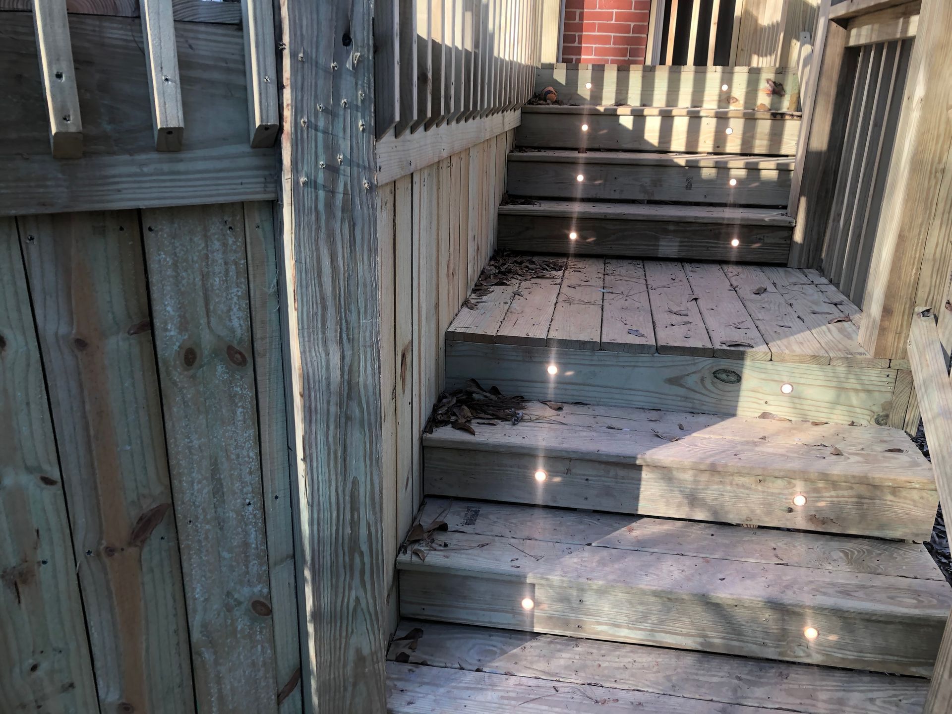 Weathered wooden outdoor stairs leading up to a deck with railing and sunlight shadows
