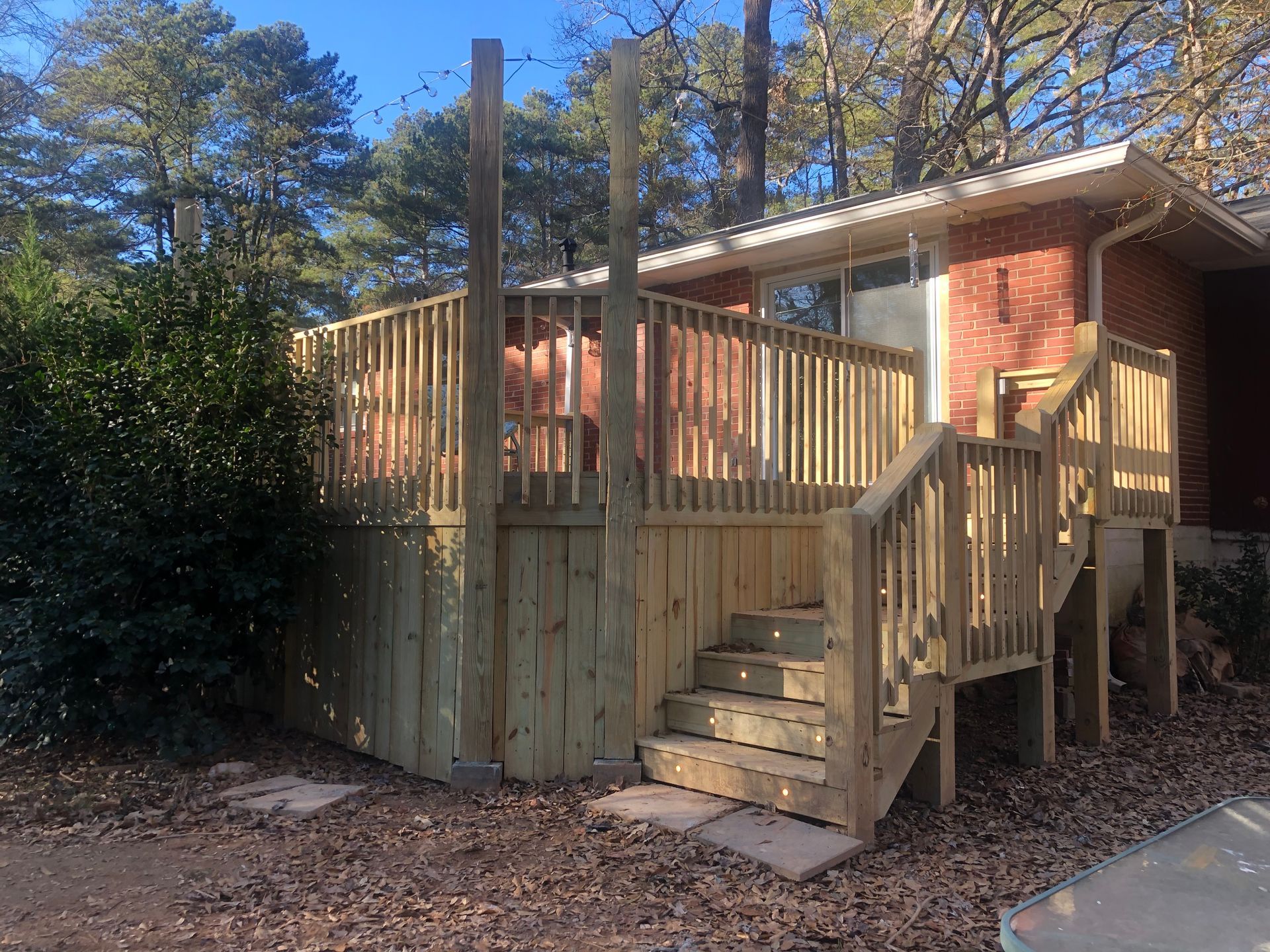 Wooden deck stairs and railing beside a brick house in a wooded yard