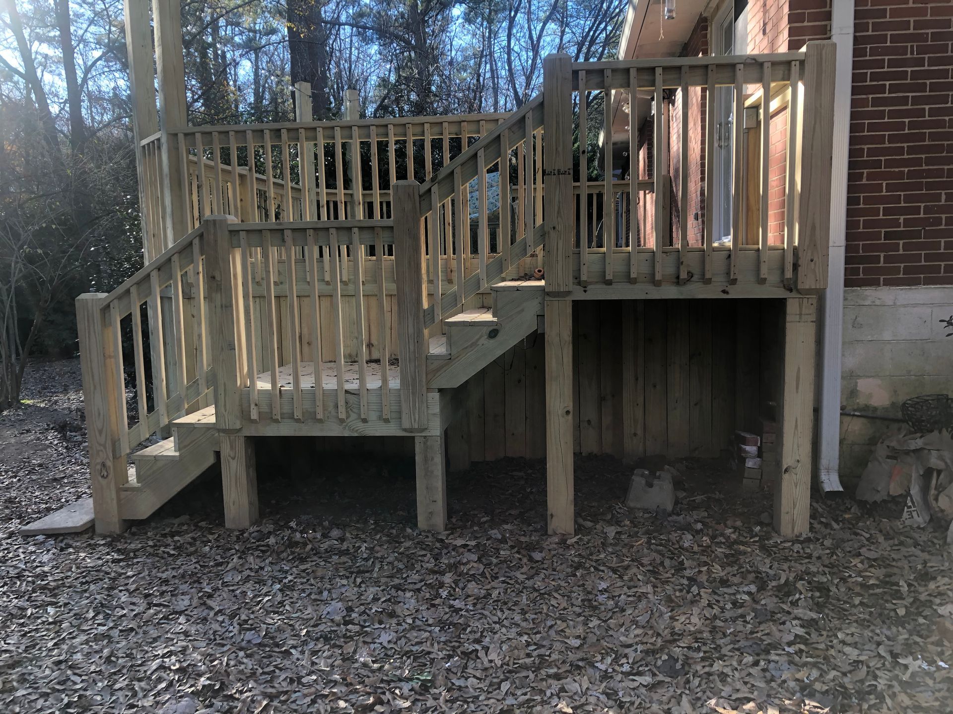 Wooden deck and stairs attached to a brick house in a wooded yard